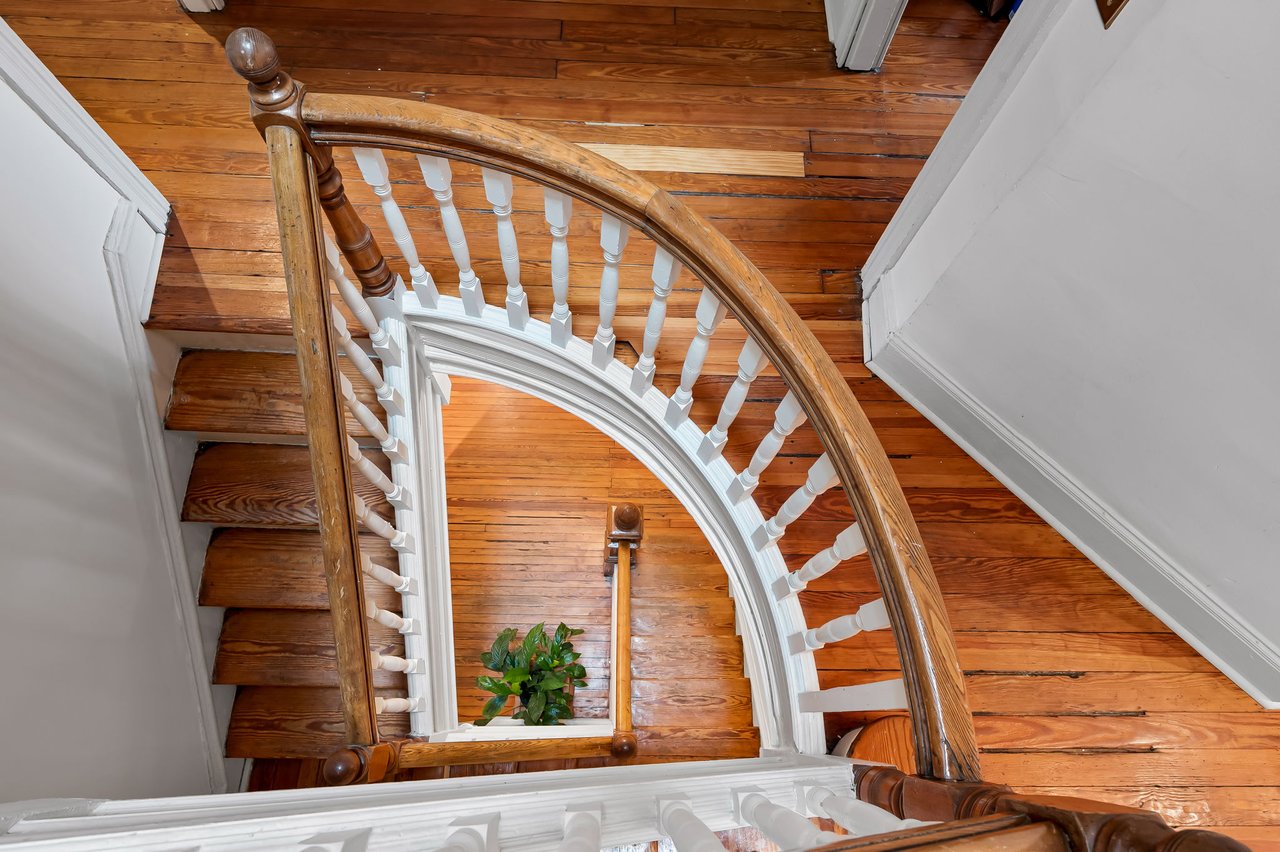 Curved wooden staircase with white balusters and polished wood floors in a historic home.