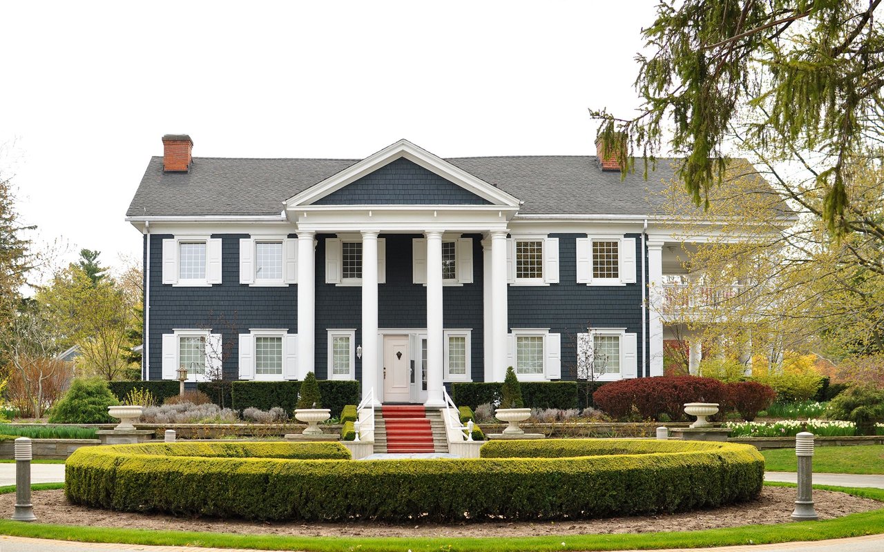 Dark blue colonial-style house with white columns, red entry steps, and a formal front garden.