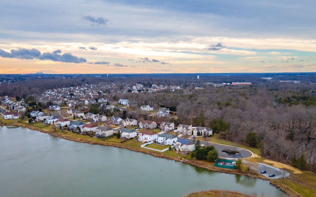 Aerial view of lakeside homes and wooded neighborhood beneath a warm sunset sky.
