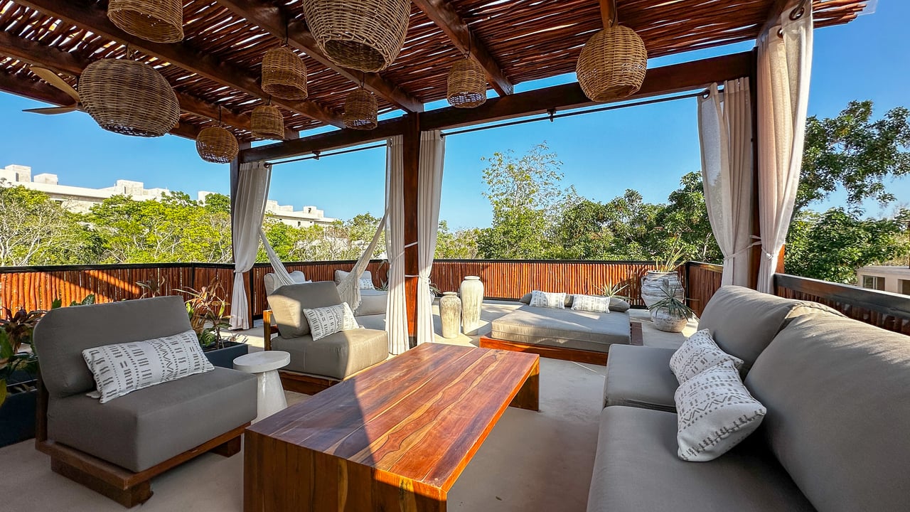 Rooftop terrace with gray lounge seating, woven pendant lights, and a timber pergola.