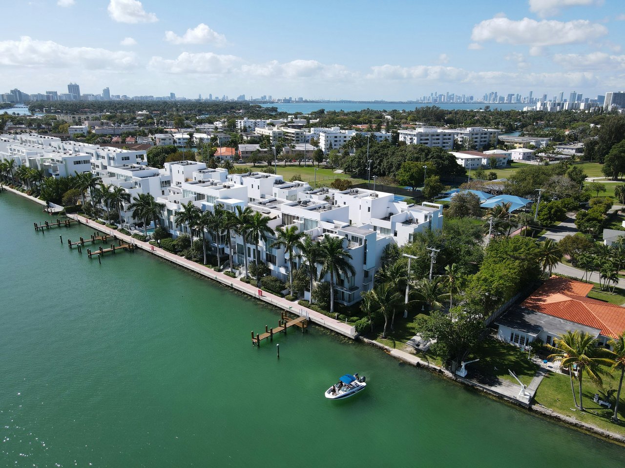 Aerial view of white waterfront homes lining a canal, with palm trees, docks, and a boat.