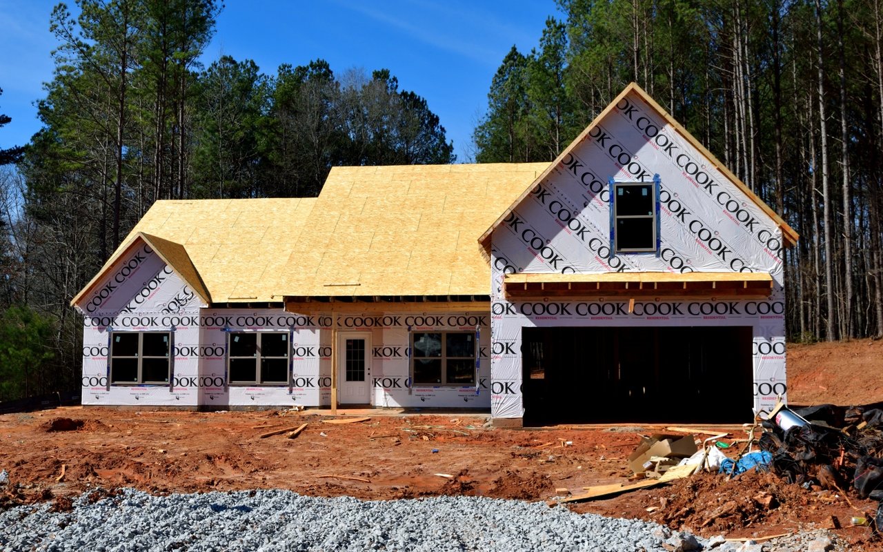 House under construction with exposed roof sheathing, printed house wrap, and an open garage.