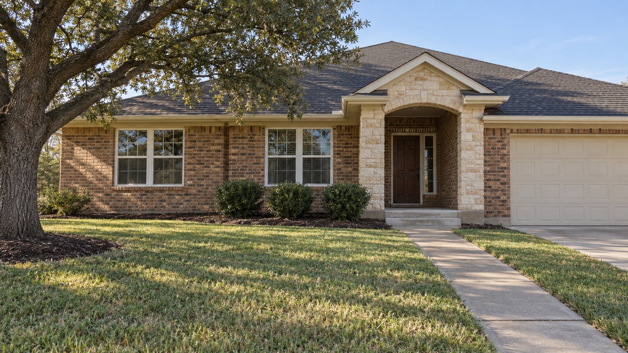 A broad front lawn and concrete walk lead to a single-story brick home with a limestone entry and mature spreading oak.