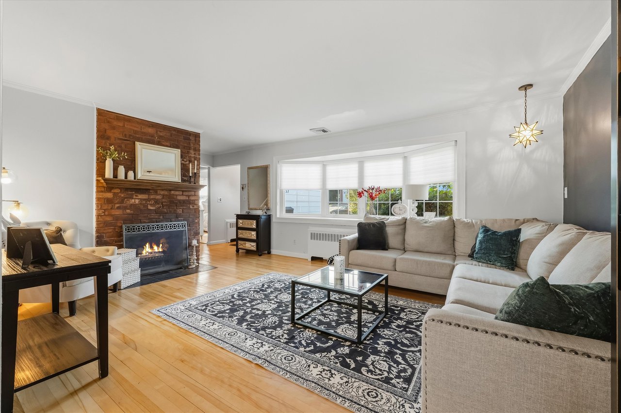 Living room with a beige sectional, patterned rug, and brick fireplace with a fire burning.