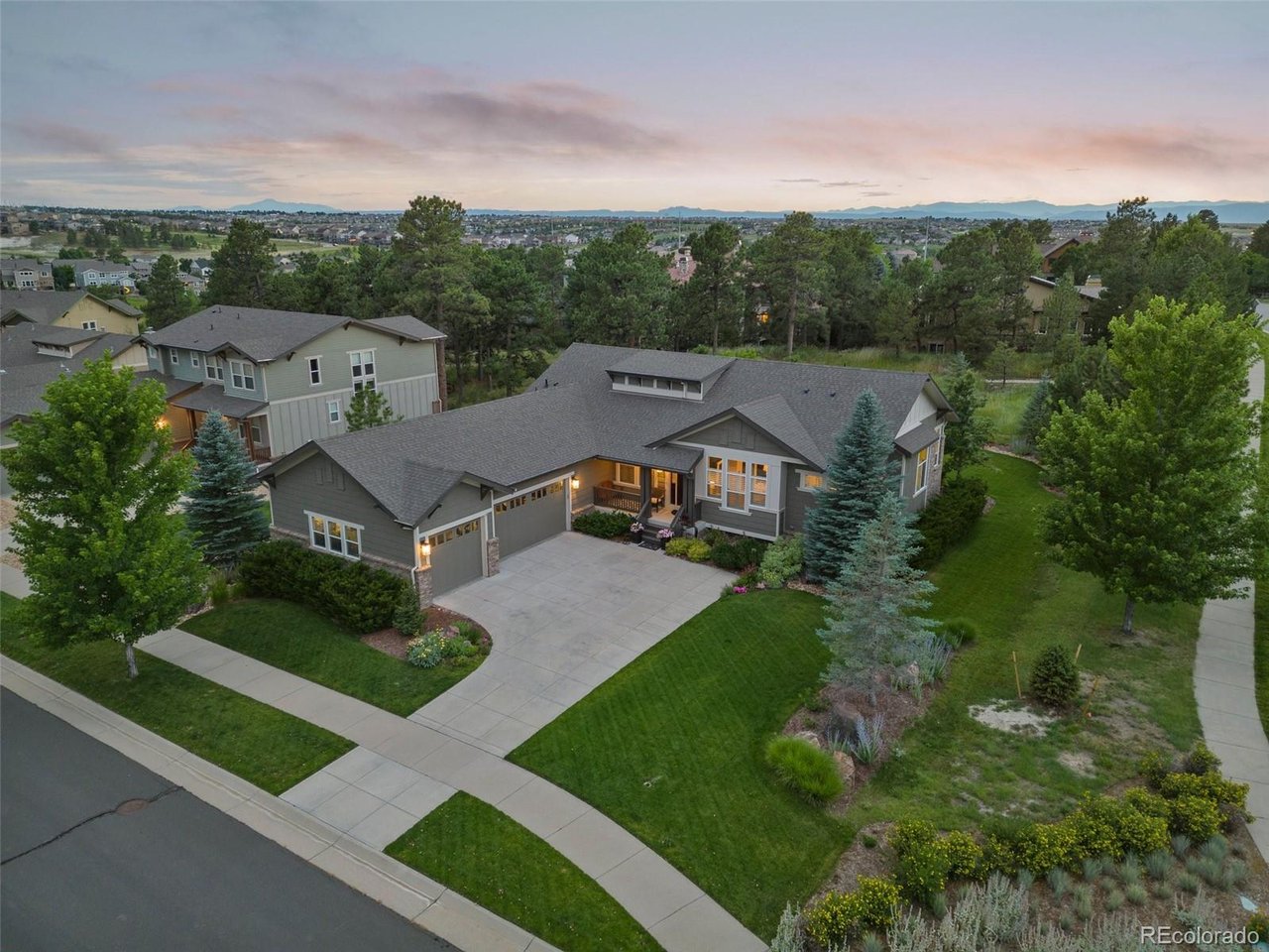 Aerial view of a gray home with a broad driveway, landscaped lawn, and distant mountains.