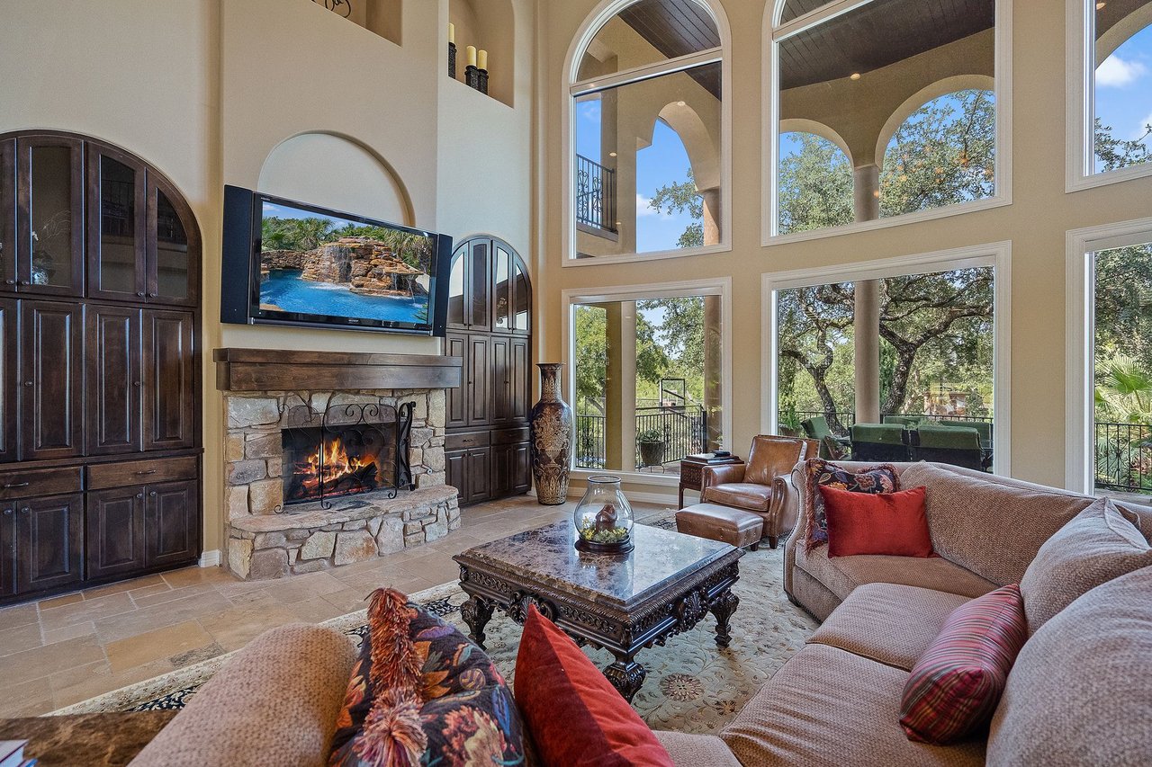 Two-story great room with floor-to-ceiling arched windows and a stone fireplace at 25715 Cliff Circle, Lakecliff on Lake Travis, Spicewood, Texas.
