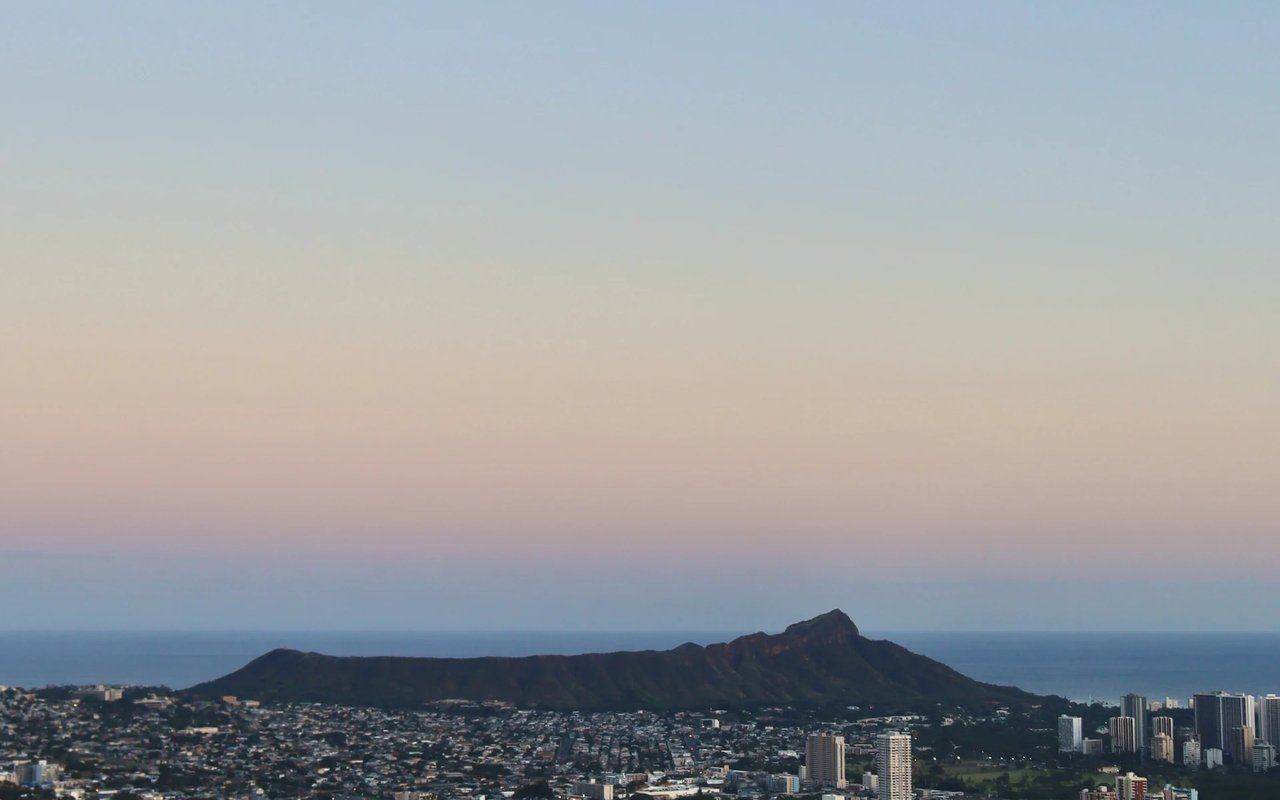Honolulu’s Diamond Head rises above the city and coastline beneath a pastel dusk sky.