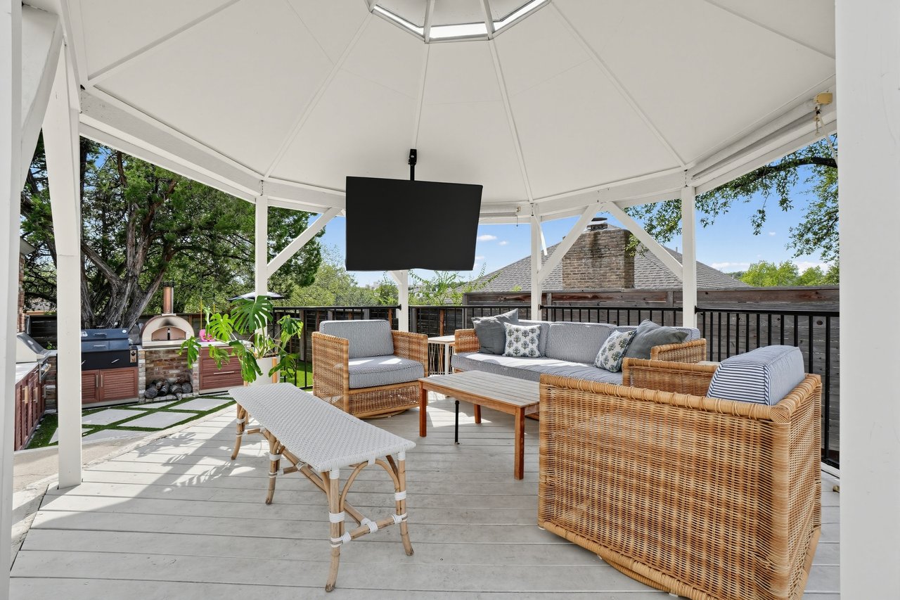 Covered patio with wicker seating, a mounted TV, and an outdoor pizza oven.