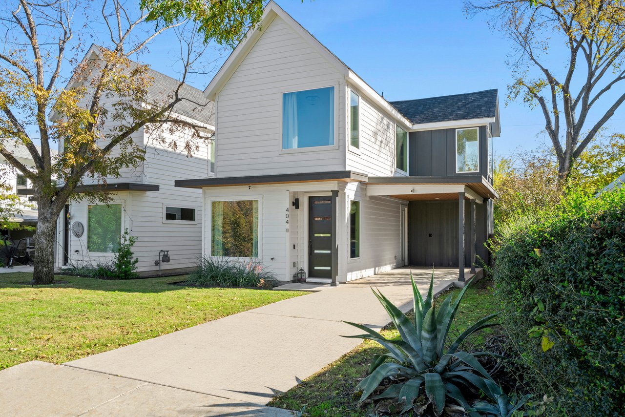 Front elevation of the modern farmhouse-style home at 404 Powell Cir Unit B in Austin's Dawson neighborhood, with white lap siding, a covered carport, and mature oak trees.