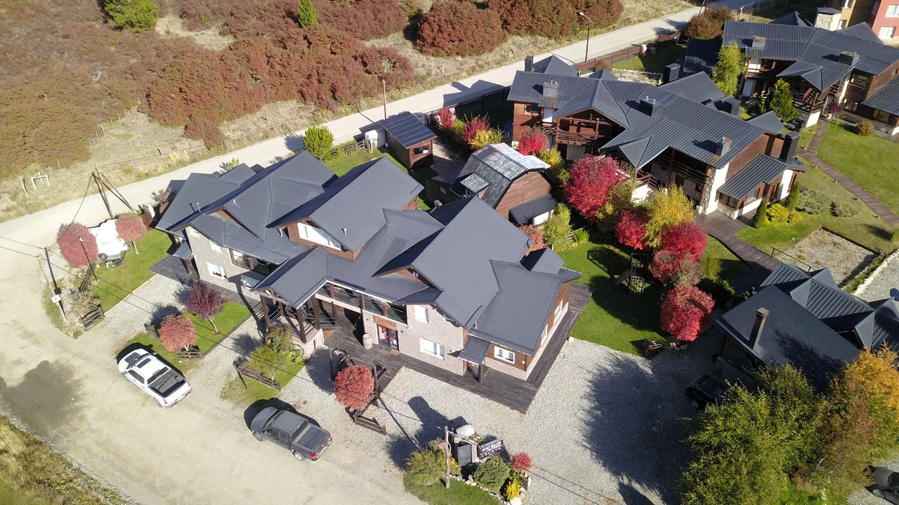 Aerial view of chalet-style buildings with dark roofs and colorful autumn trees.