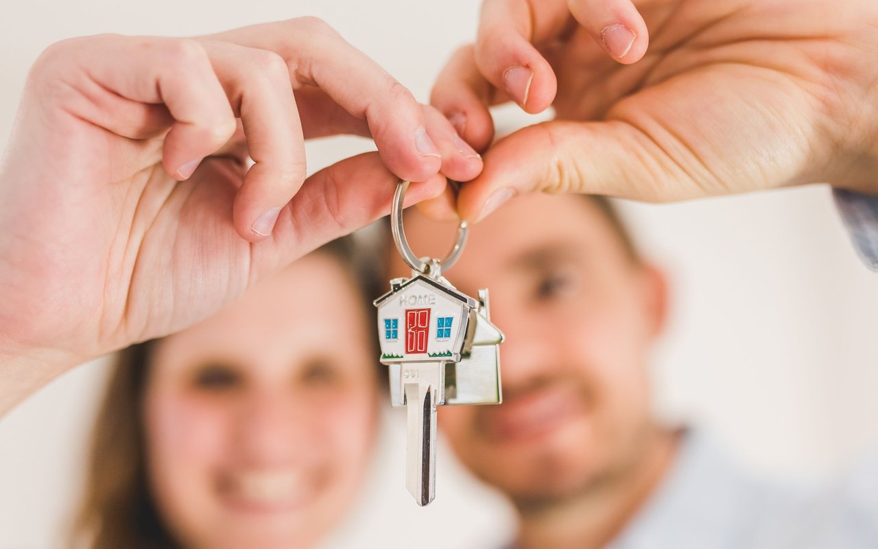 A smiling couple receives keys with a small house-shaped keychain.
