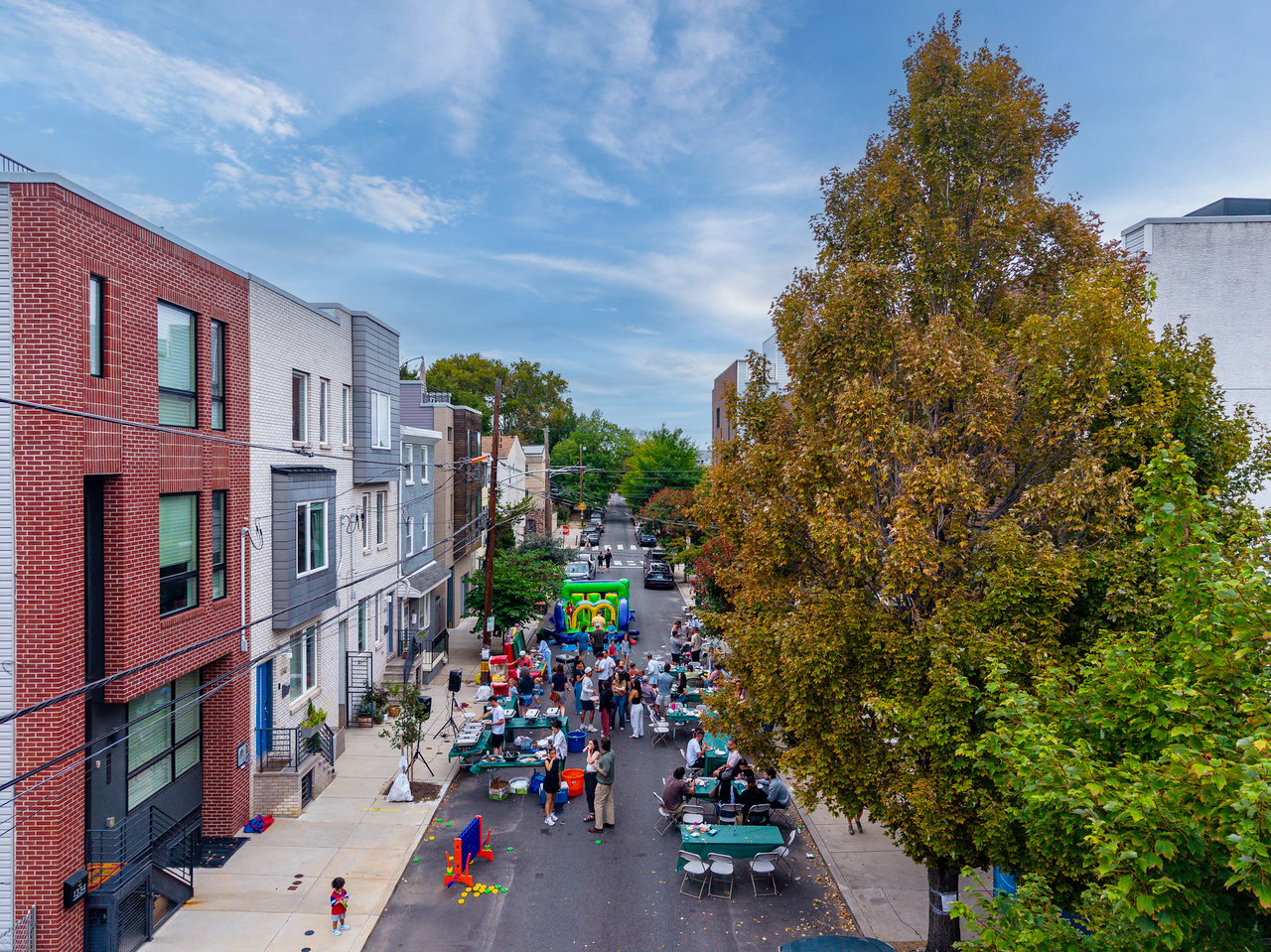 Neighbors gather at a residential street block party with tables and a colorful bounce house.