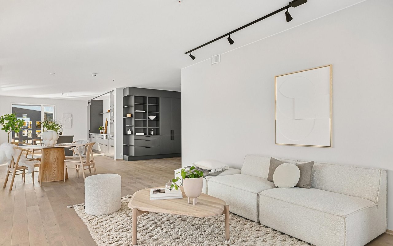 Open-plan living and dining room with a white sectional, pale wood furniture, and dark kitchen cabinetry.