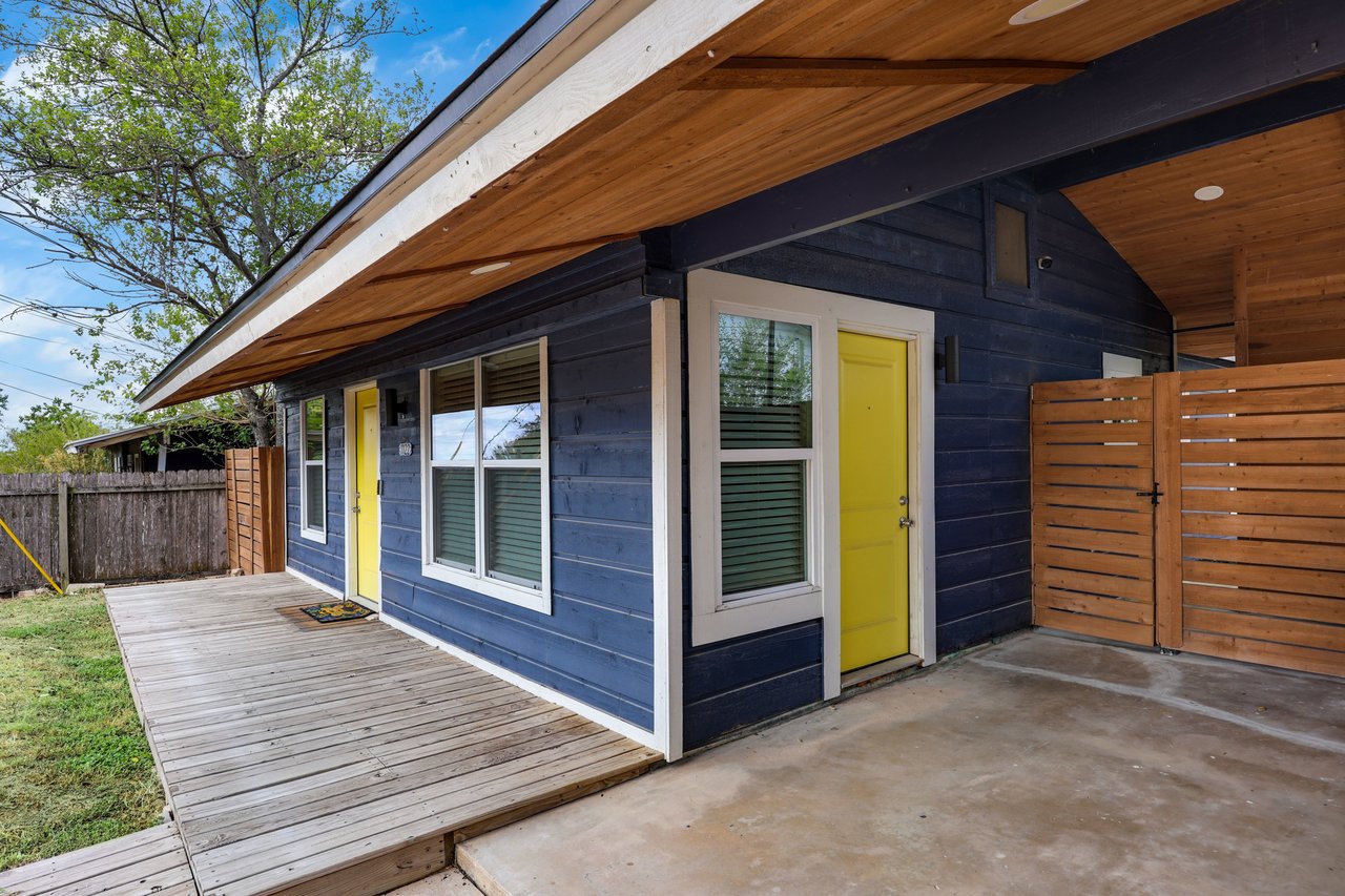 Blue home with yellow doors, a long wood deck, and a covered patio.