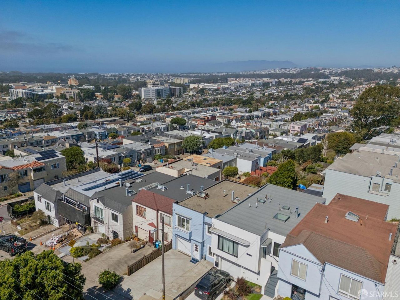 Aerial view over neighborhood rooftops toward the city and distant hills.