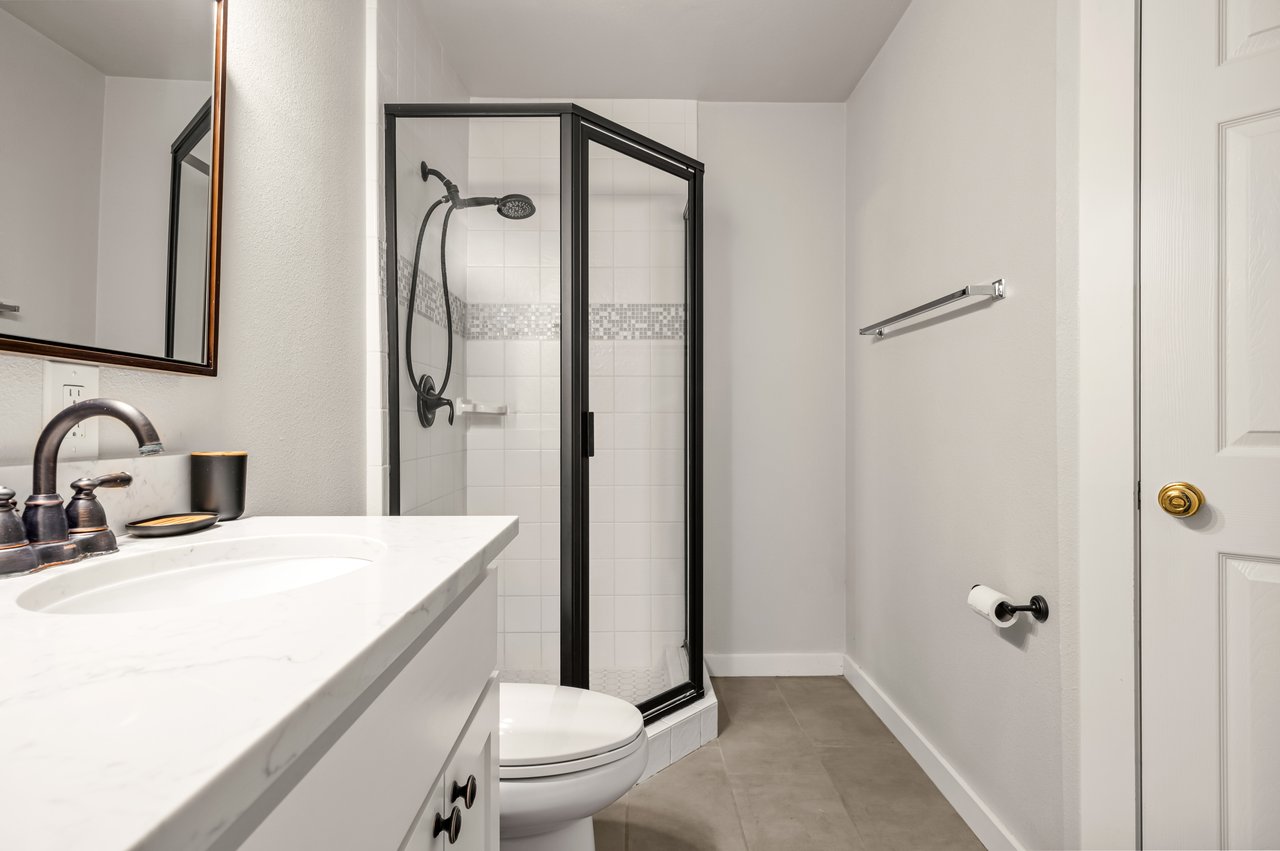 Bathroom with a black-framed glass shower, white vanity, and gray tile floor.