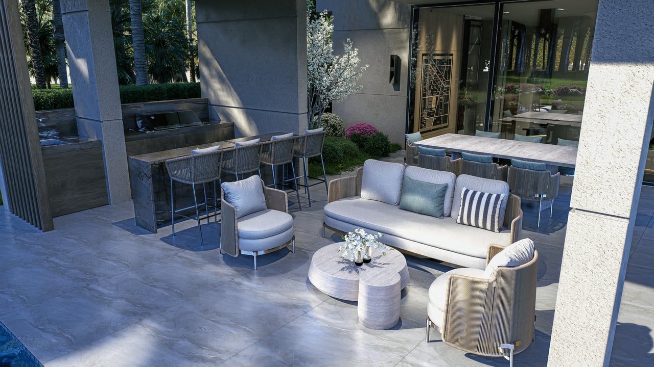 Furnished stone patio with a cushioned lounge area, bar seating, and a glimpse of the pool.
