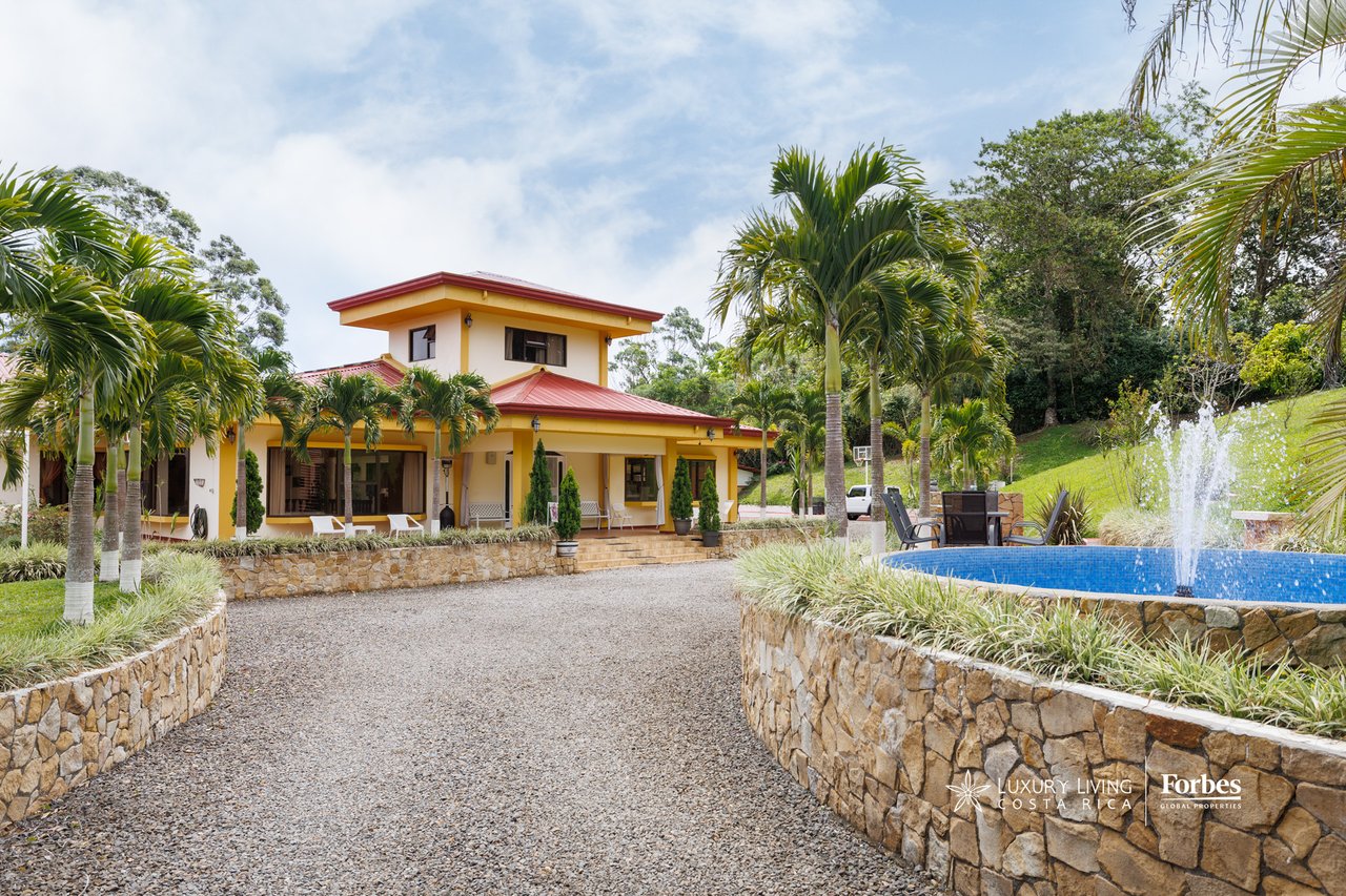 Yellow two-story house with red roofs, palm trees, and a swimming pool with fountain.