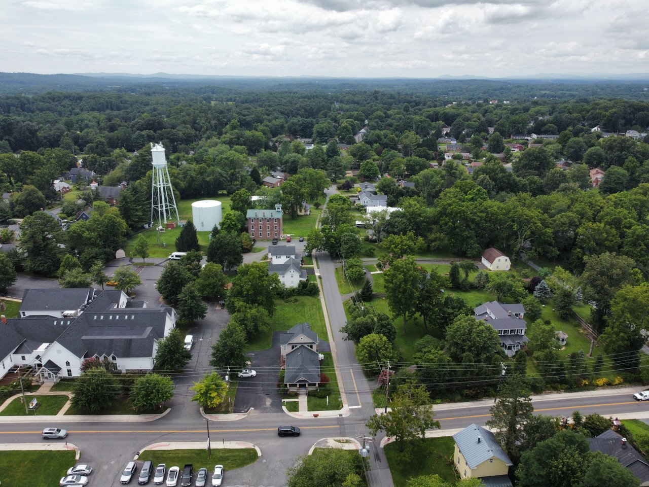 An elevated aerial drone shot capturing the historic residential streets, mature tree canopy, and rolling countryside surrounding Hamilton, VA in Western Loudoun County, photographed by local real estate expert Diana Geremia.