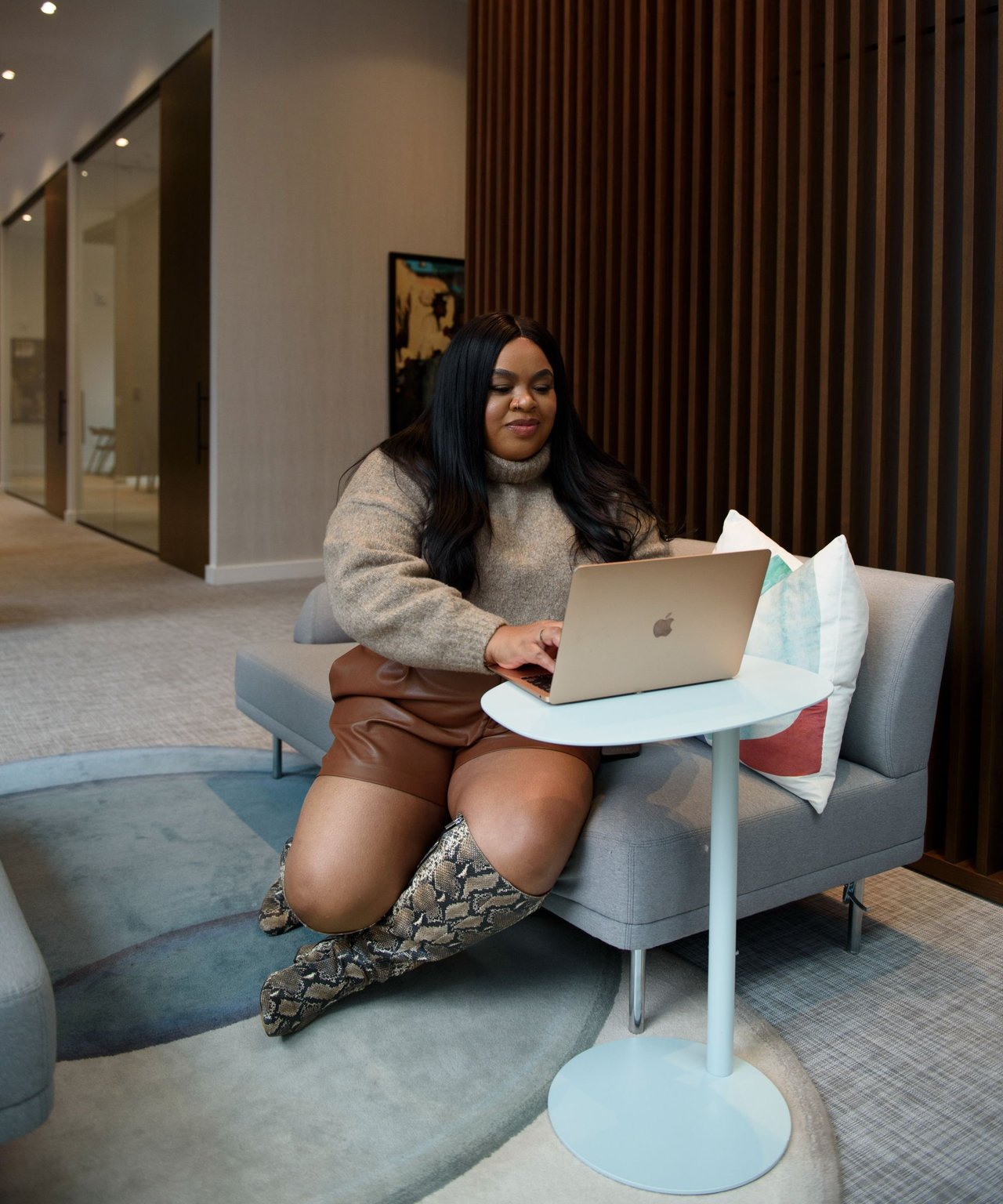 Janay Cheek works on a laptop while seated on a sofa in an office lounge.