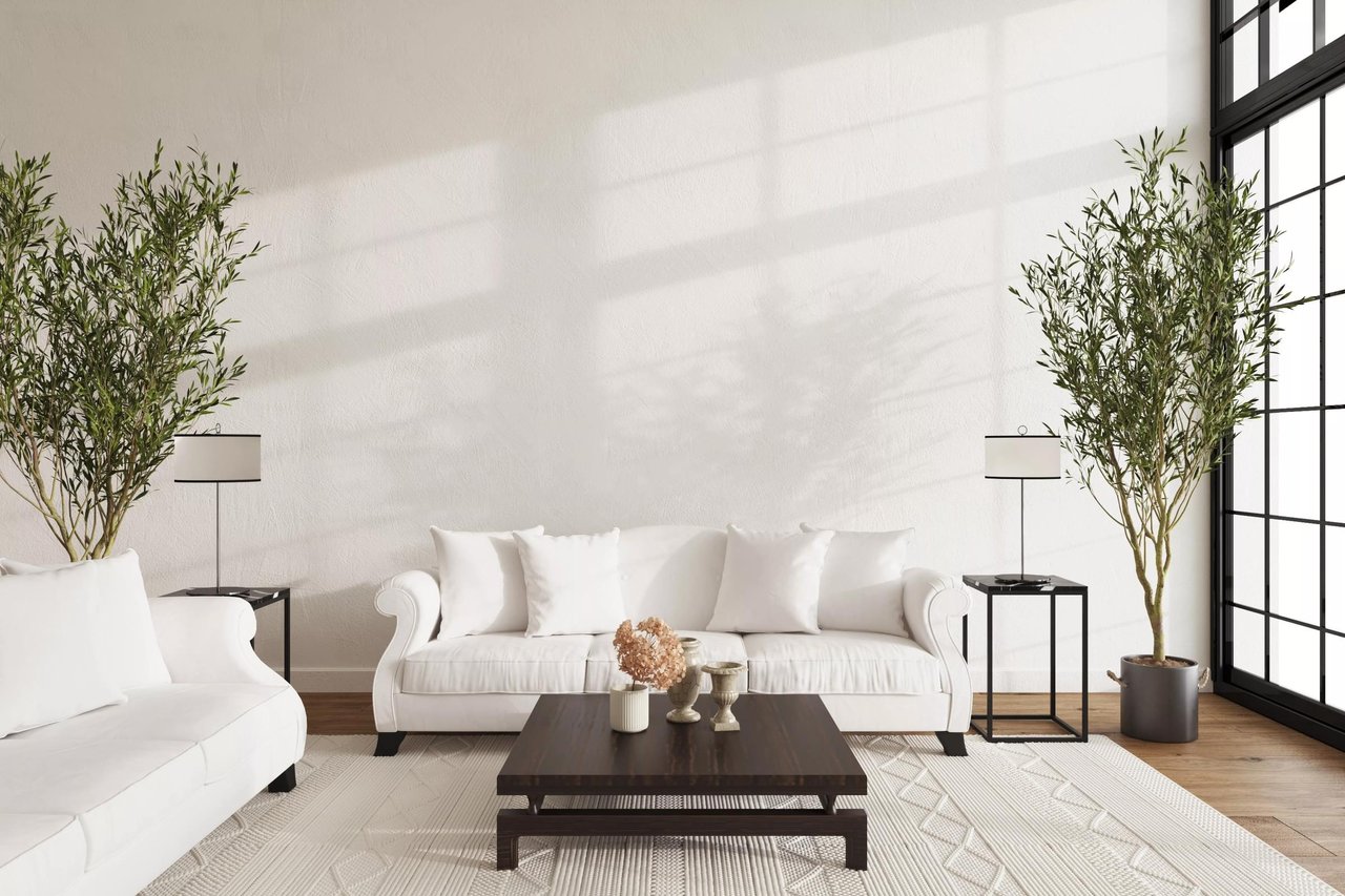 Bright living room with white sofas, a dark coffee table, and tall trees beside black-framed windows.