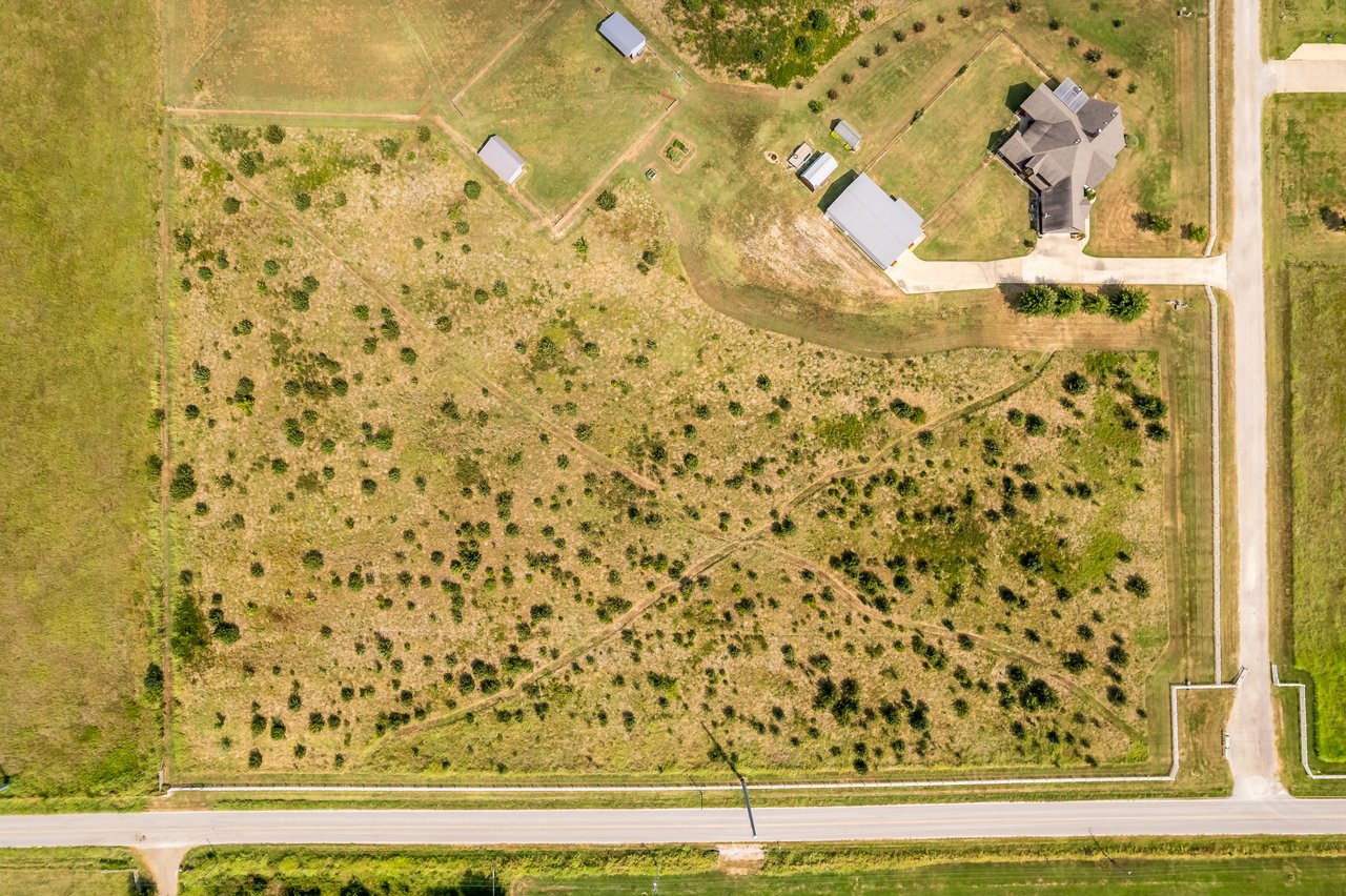 Aerial view of open acreage with a house, outbuildings, and roads along two sides.
