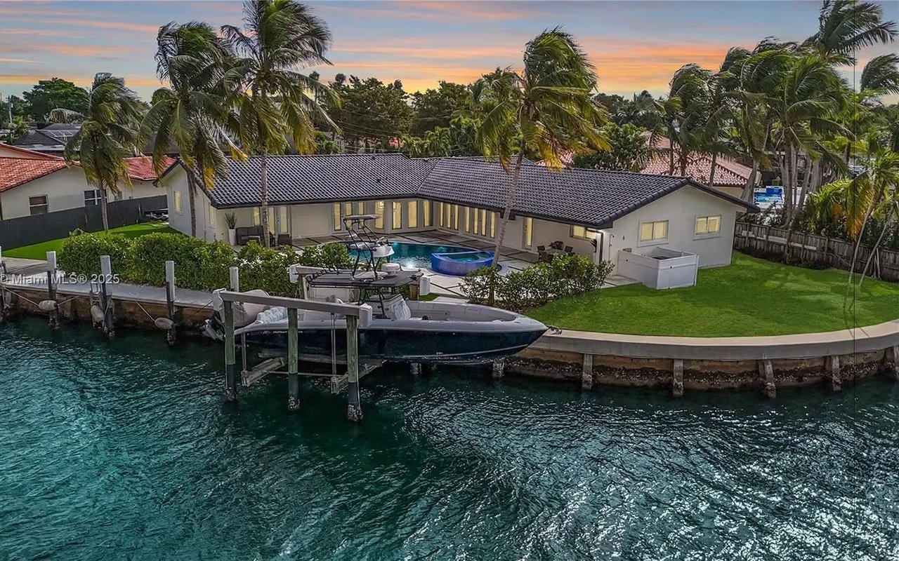 Waterfront home with a private dock, boats, pool, and palm trees at sunset.