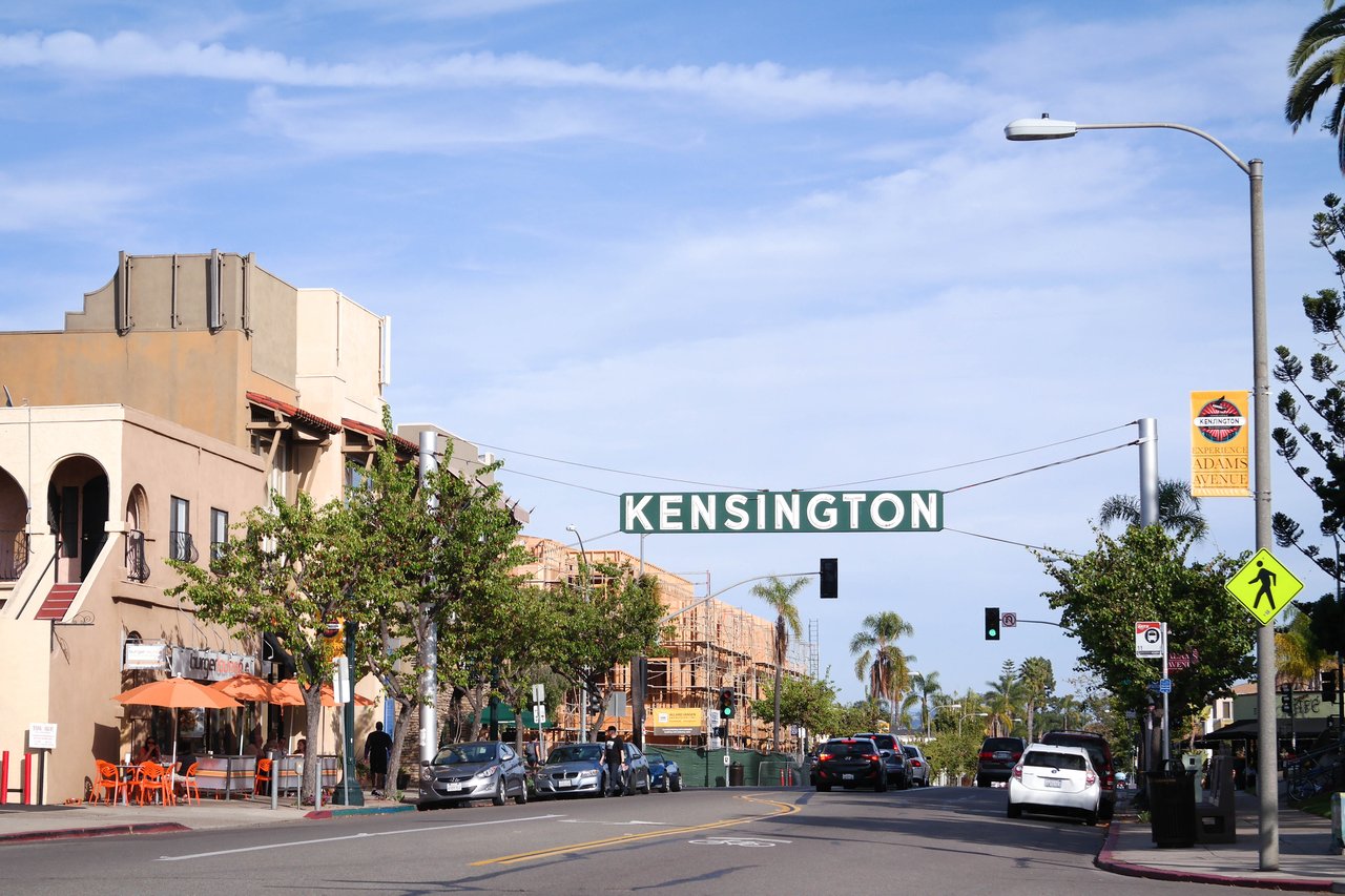 The Kensington neighborhood entrance sign above Adams Avenue, with local shops, restaurants, and walkable streets that showcase the area's community-focused charm and historic architecture.