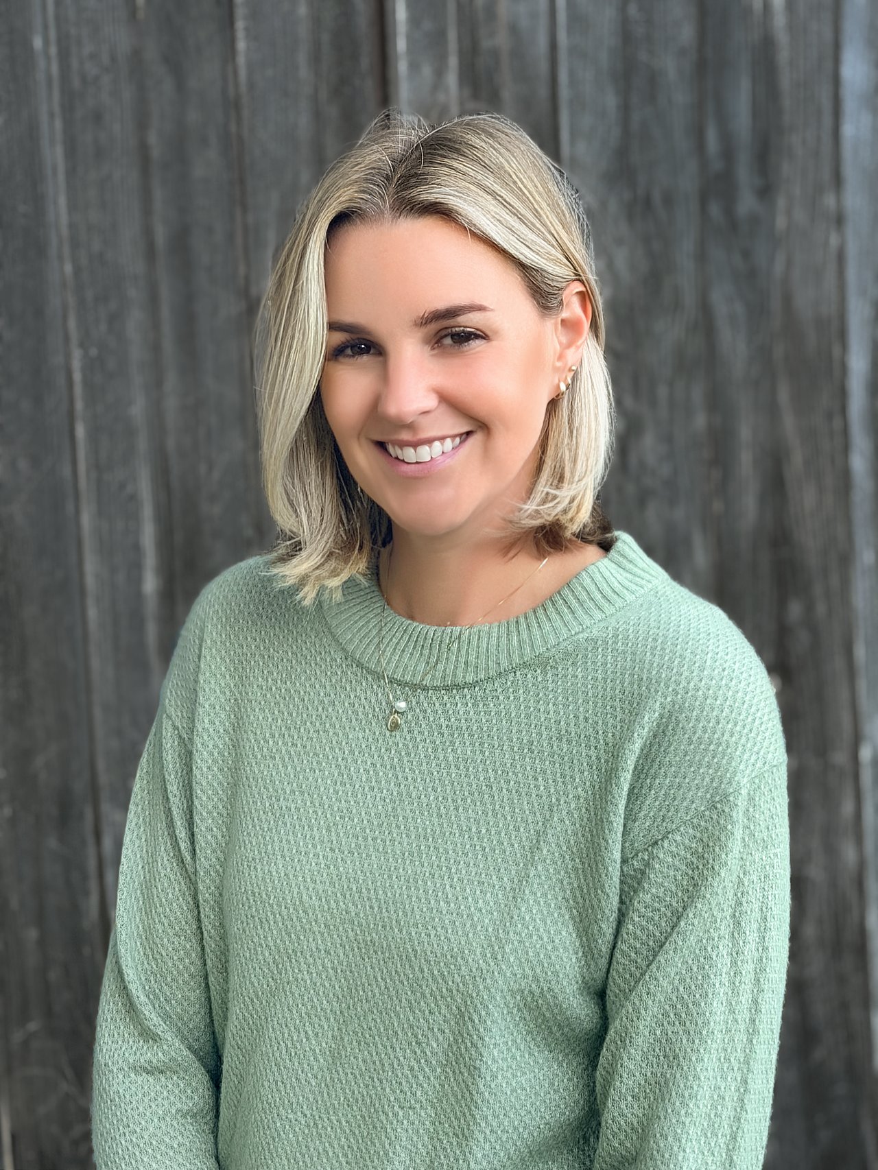 Hillary Wheeler smiling in a mint-green sweater against a dark wooden backdrop.