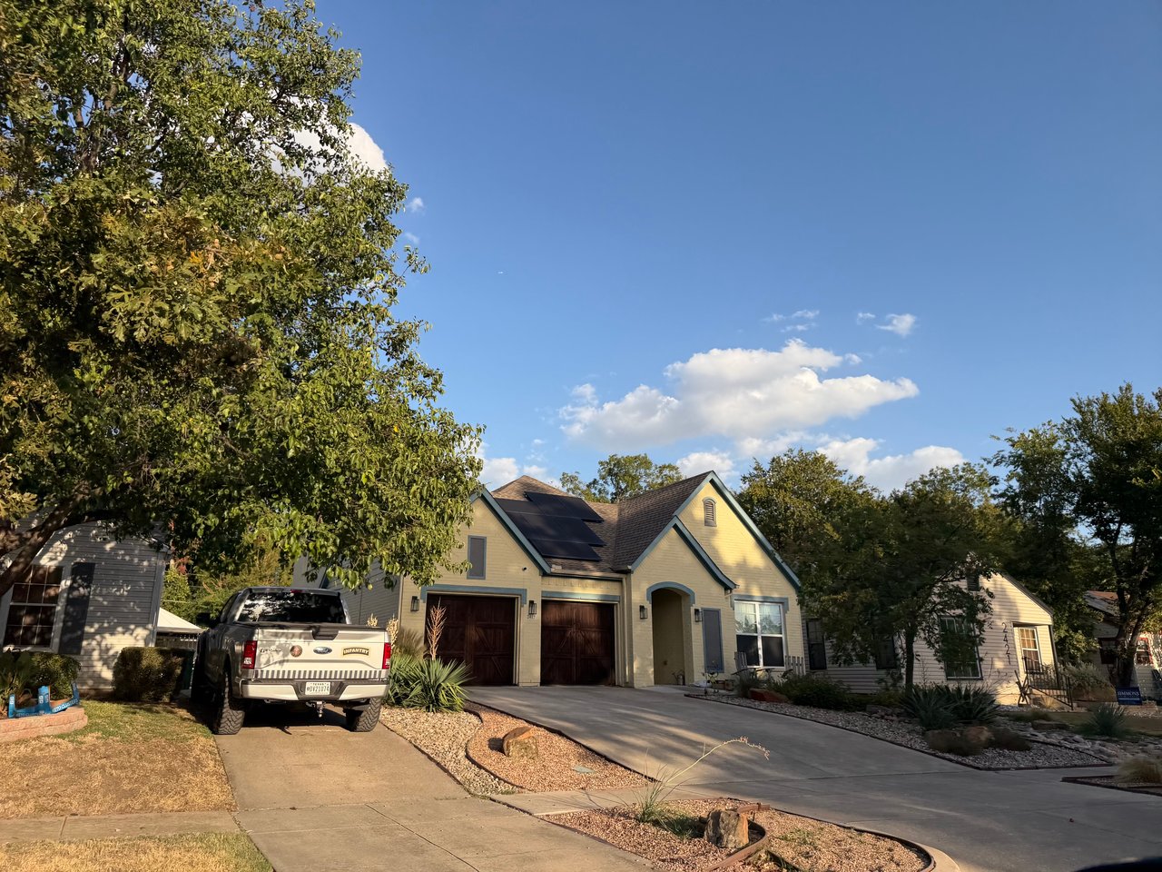 Pale yellow gabled home with solar panels, a two-car garage, and a pickup in the driveway.