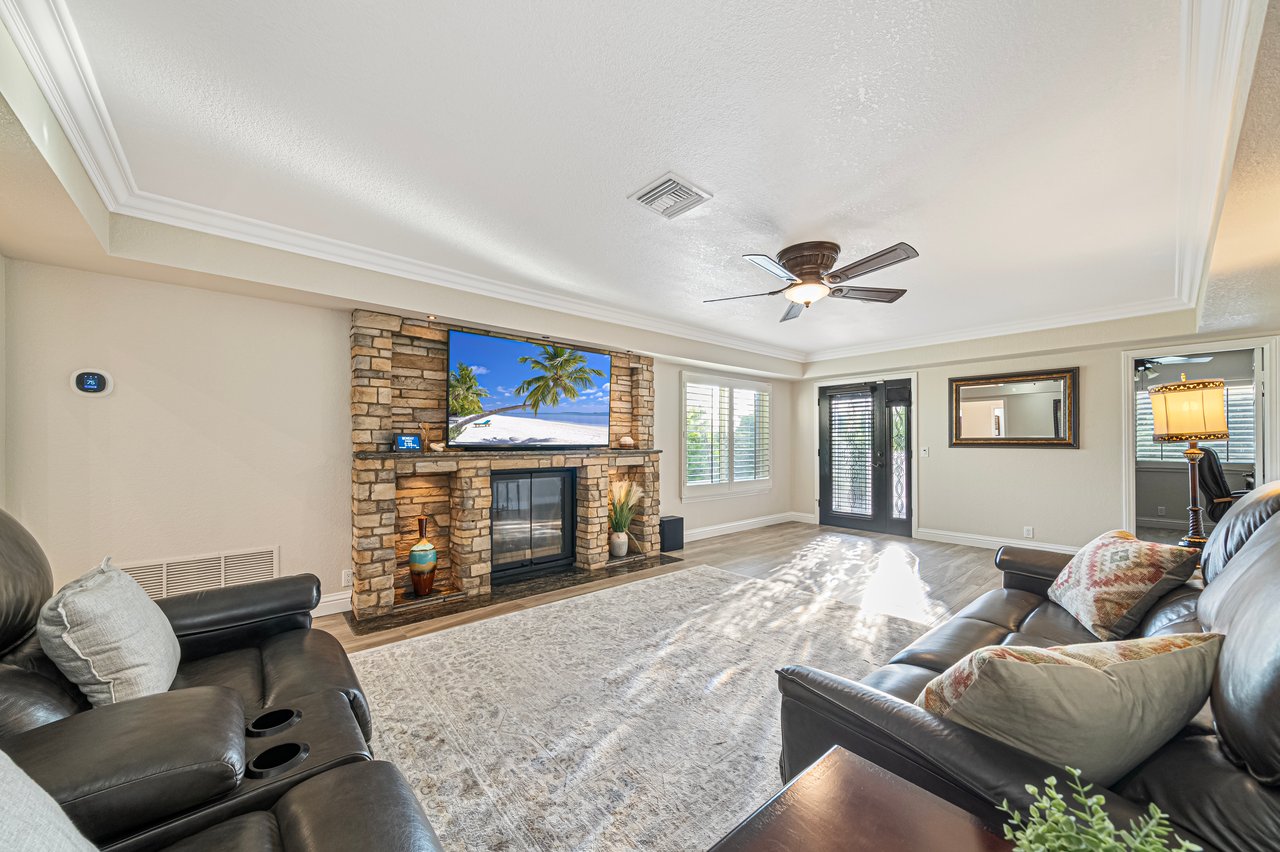 Living room with a stone fireplace, leather sofas, and sunlight across a large area rug.