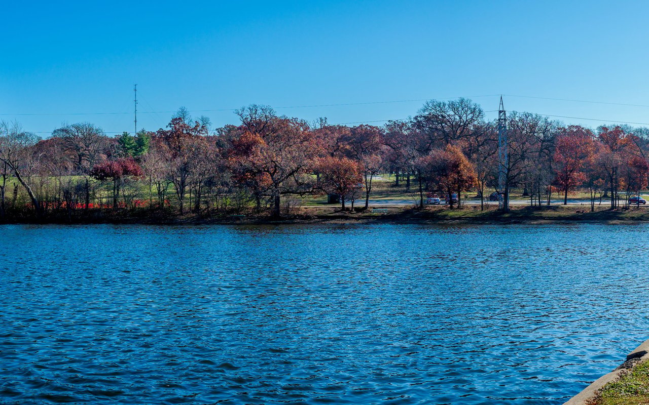 Lake bordered by autumn trees, with a road and utility poles along the far shore.