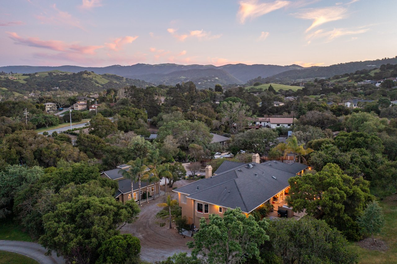 Aerial view of tree-lined homes and rolling hills beneath a pink sunset sky.