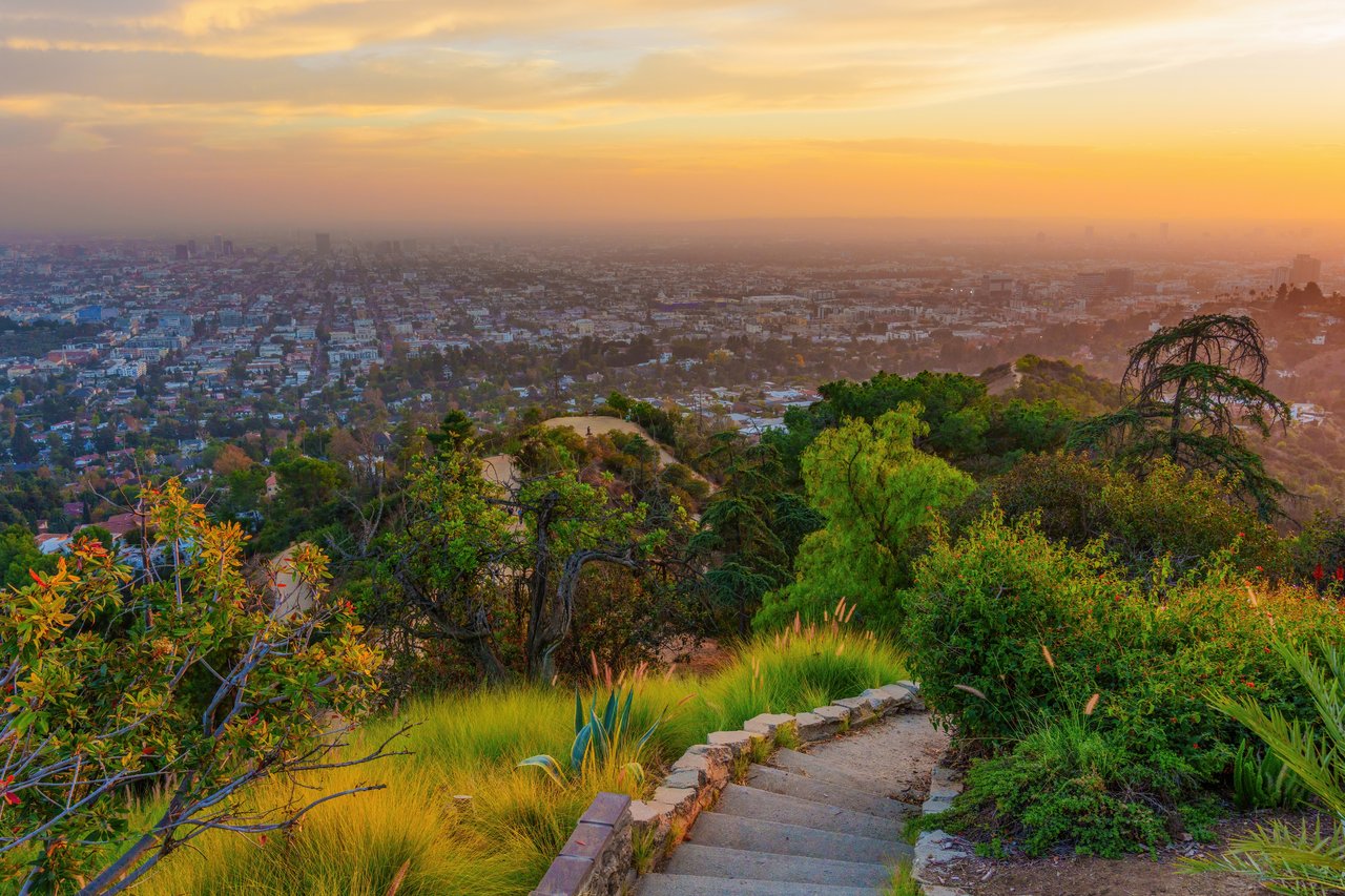 Los Angeles skyline at sunset viewed from a hillside staircase.