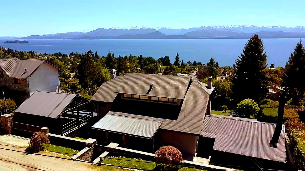 Casa Gral Roca above a lake, with snow-dusted mountains across the water.