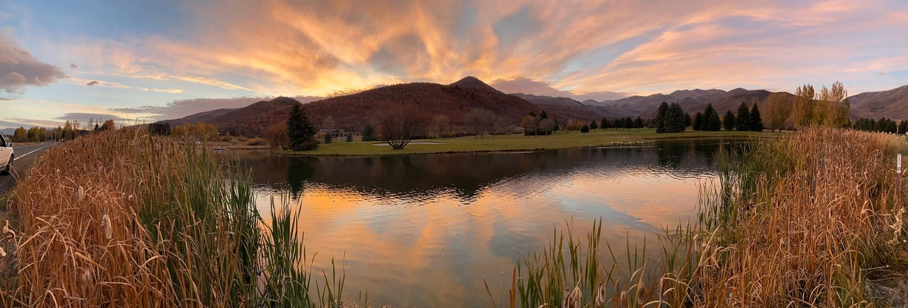 Reed-lined pond reflects a sunset sky beneath a distant mountain range.