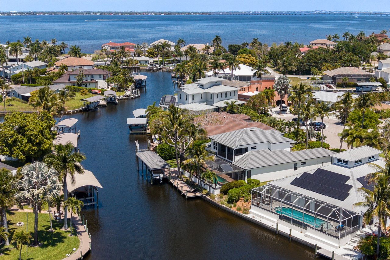 Aerial view of canal-front homes and docks, with a screened pool and bridge across the bay.