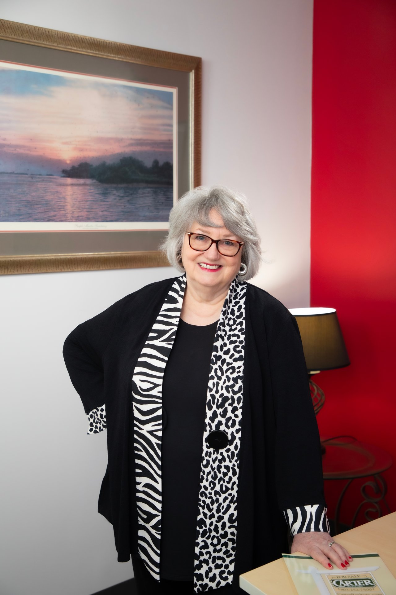 Margaret-Ann Ashburn smiles in her office, wearing glasses and a black-and-white patterned scarf.
