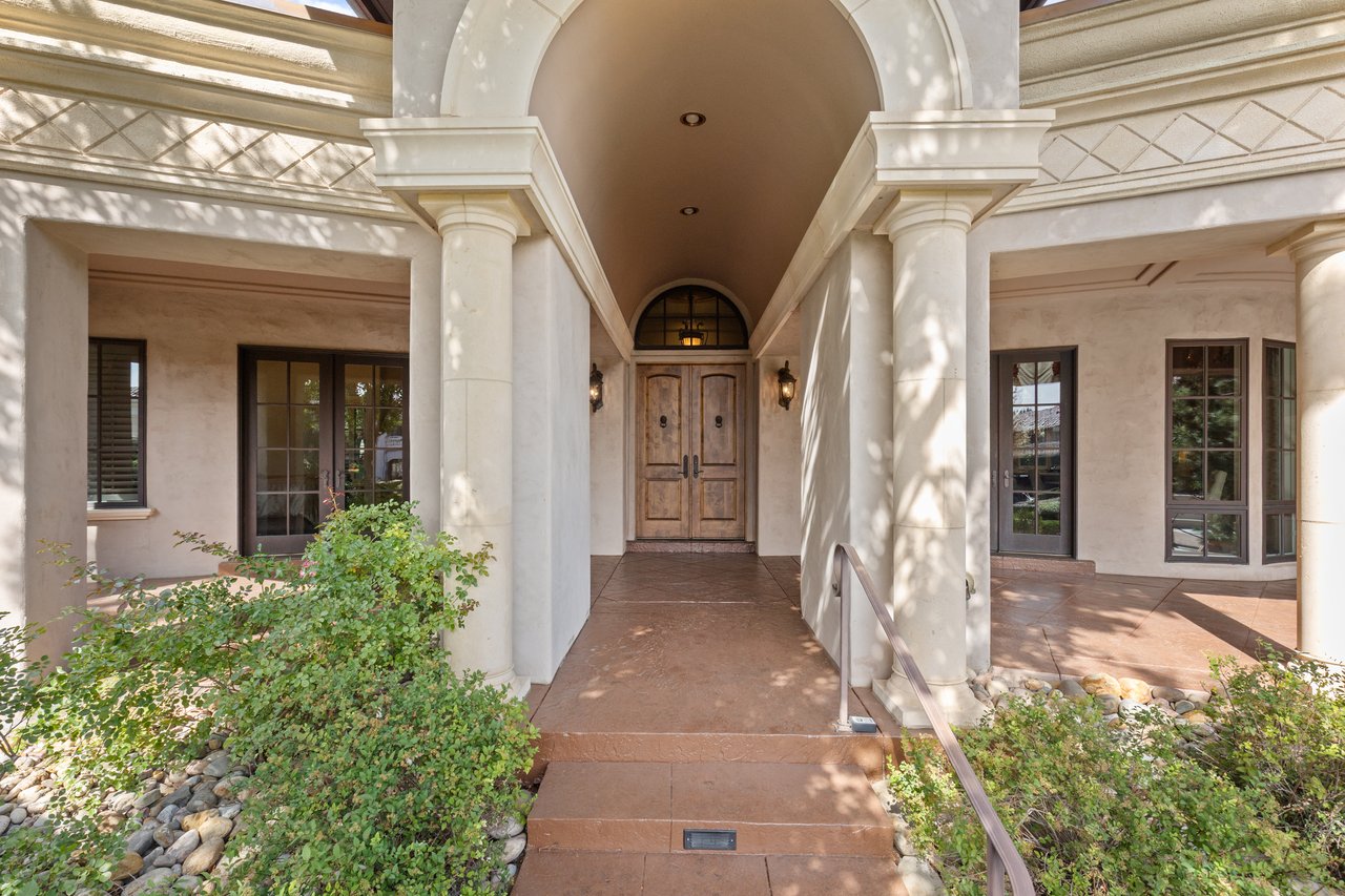 Guest house entrance with white columns, an arched covered walkway, and wooden double doors.