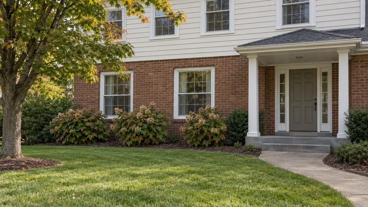 Brick and ivory-clapboard home with a sheltered front entrance, curved concrete walk, deep lawn, and autumn-edged planting.