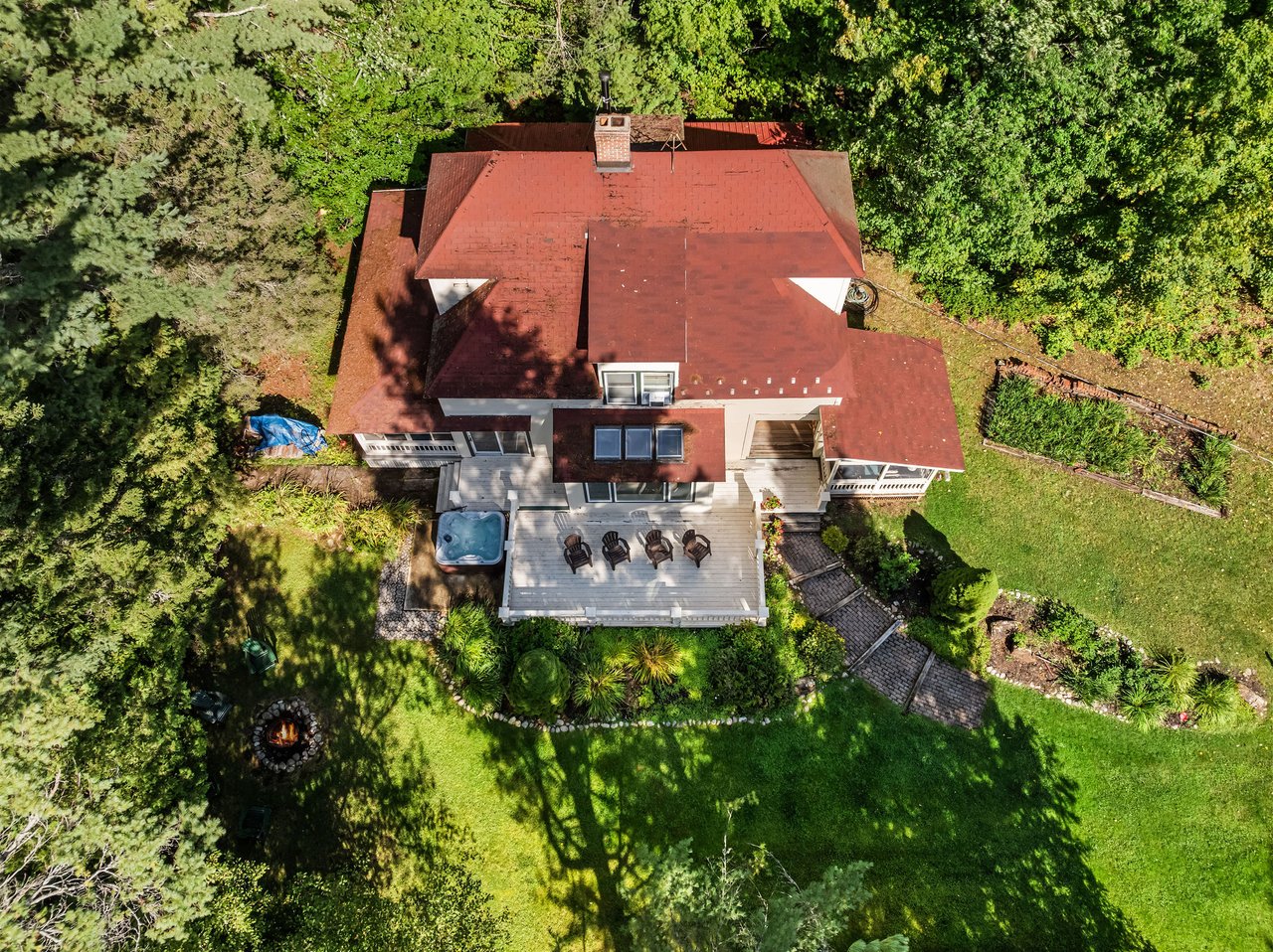 Aerial view of a red-roofed house with a deck and hot tub surrounded by trees and lawn.