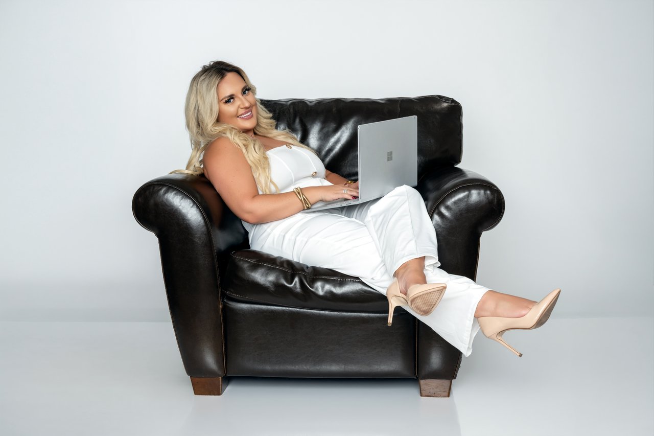 Woman in white seated in a black leather armchair with a laptop