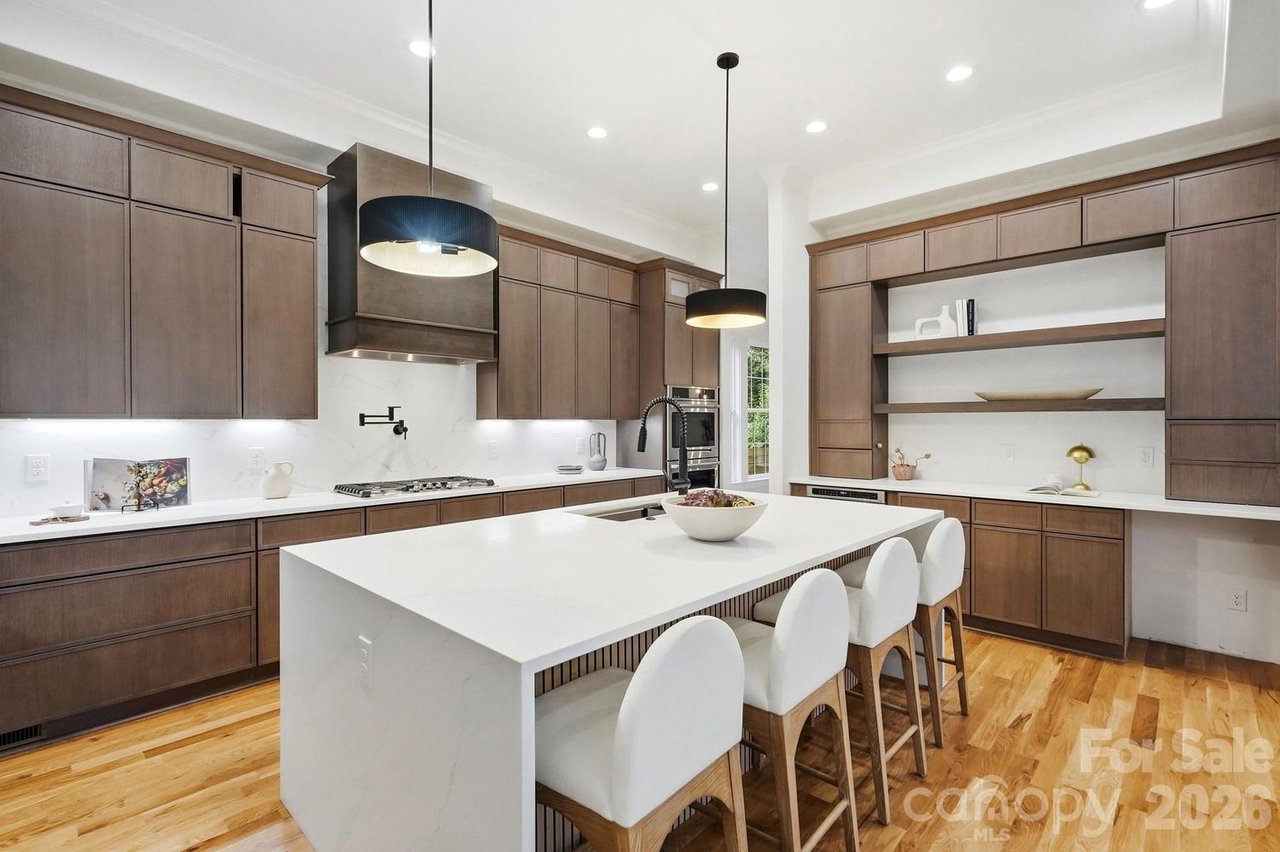 Modern kitchen with dark wood cabinetry, white waterfall island, and a row of bar stools.