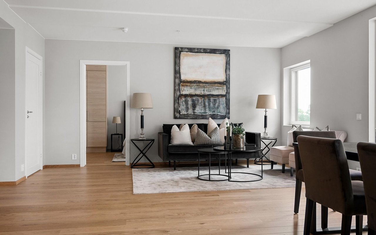 Living room with a black sofa, abstract artwork, light wood floors, and a dining area.