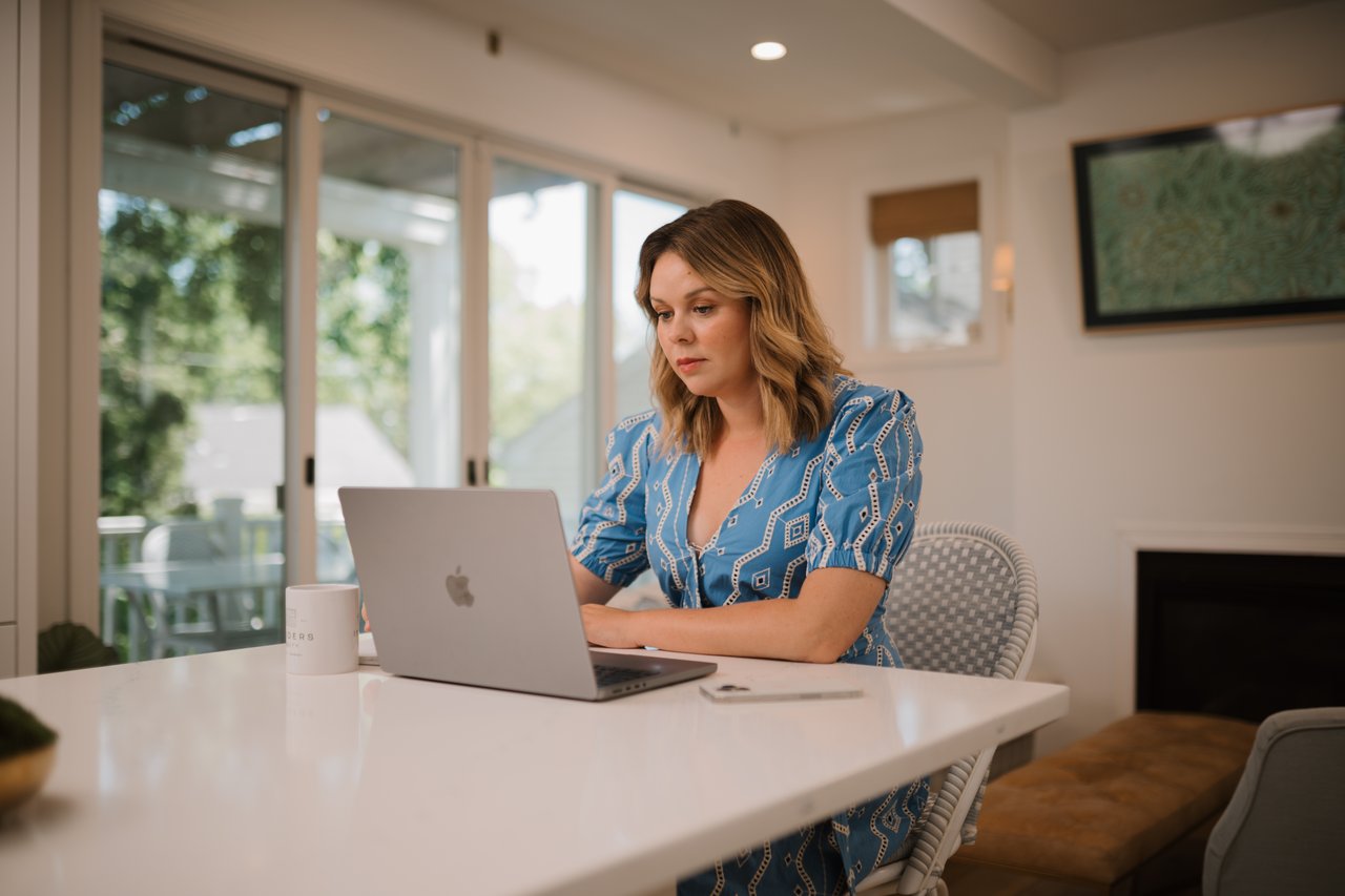 Cait Berry of Insiders Realty working on a laptop at a kitchen counter in a bright Madison-area home.