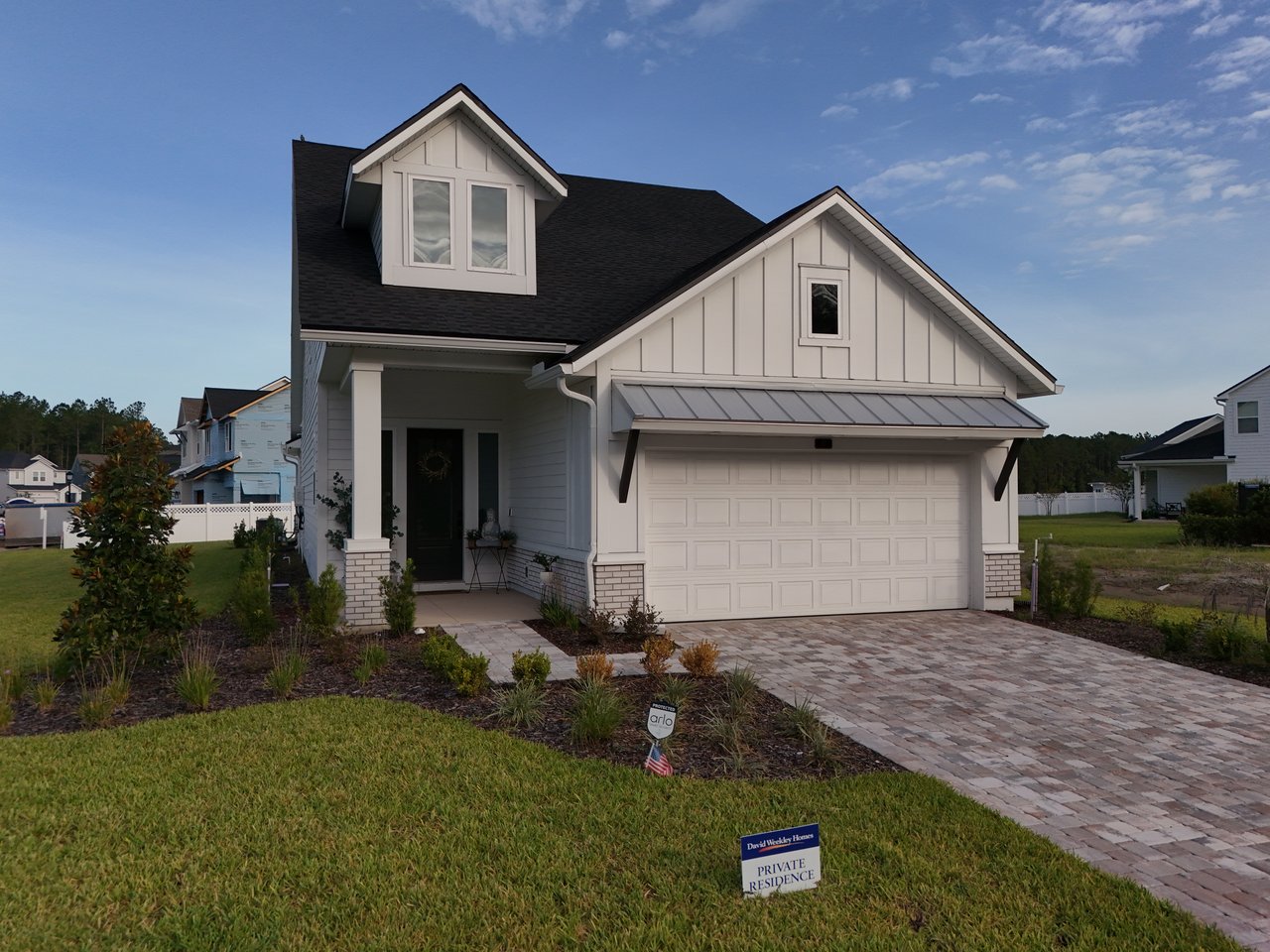 White home with prominent gables, an attached garage, and a wide paver driveway.