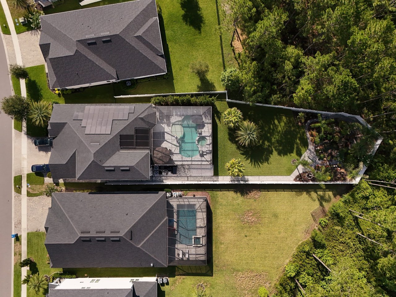 Aerial view of Silverleaf Village homes, with screened pools, solar panels, and lawns beside wooded grounds.