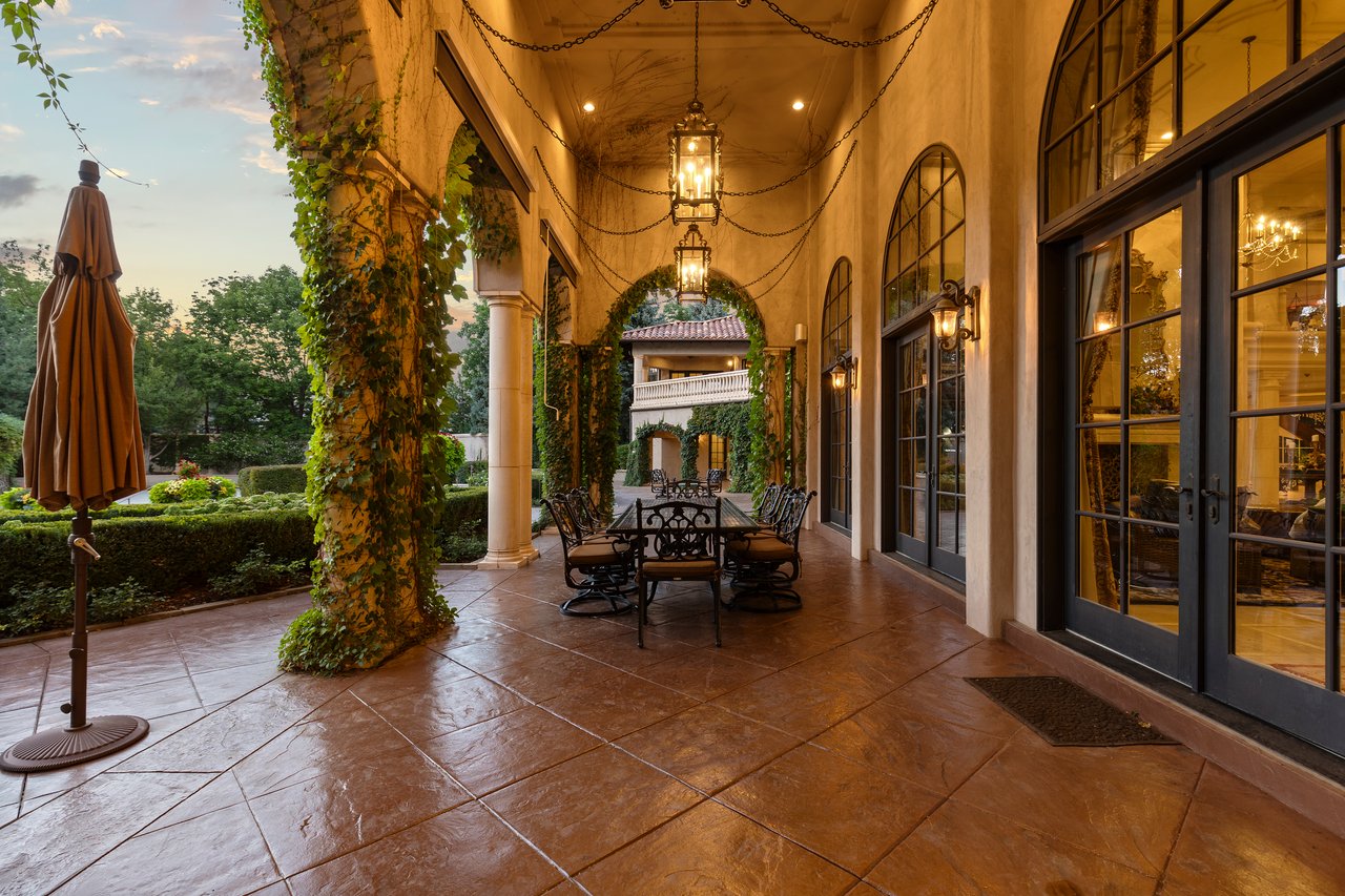 Covered courtyard patio with ivy-covered arches, hanging lanterns, and a wrought-iron dining set.