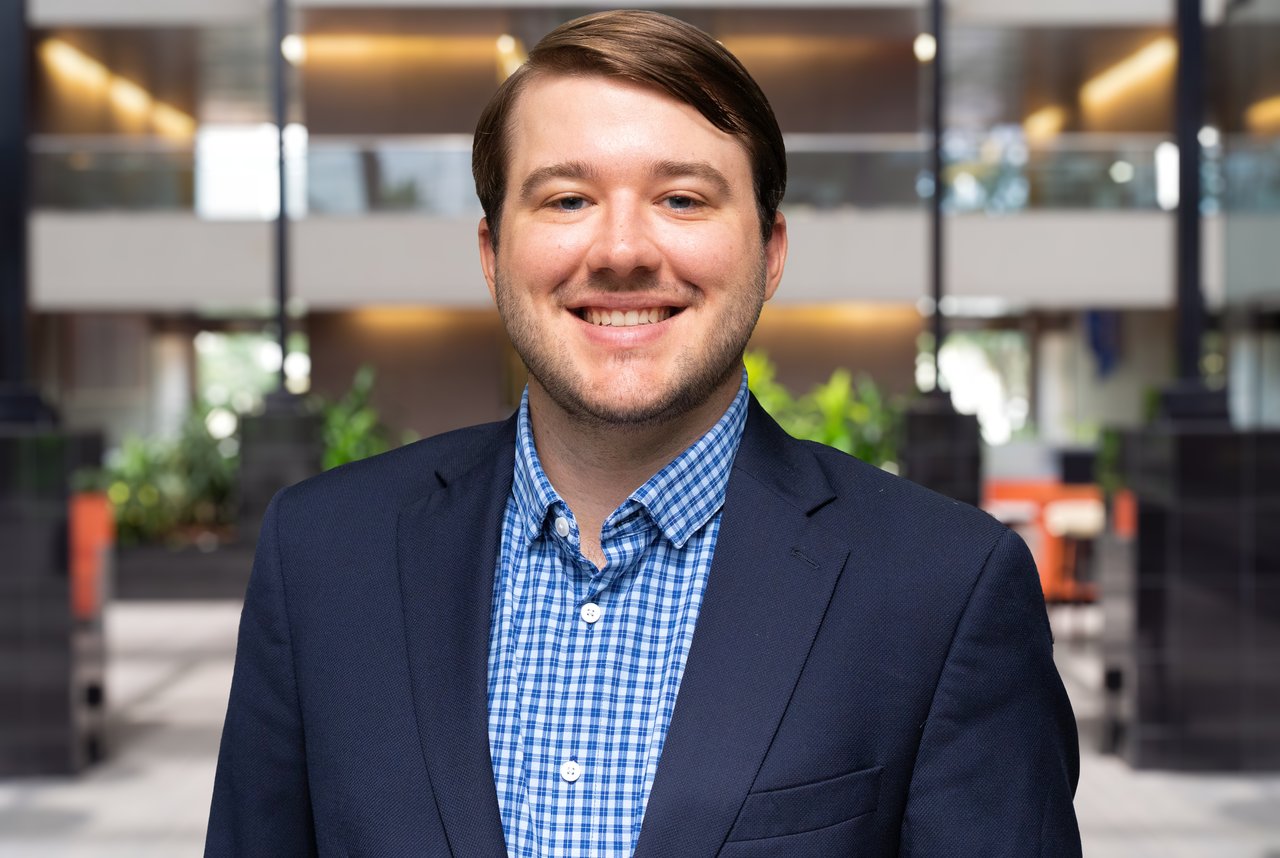 Benjamin Nicknish smiling in a navy blazer and blue checkered shirt in an office.