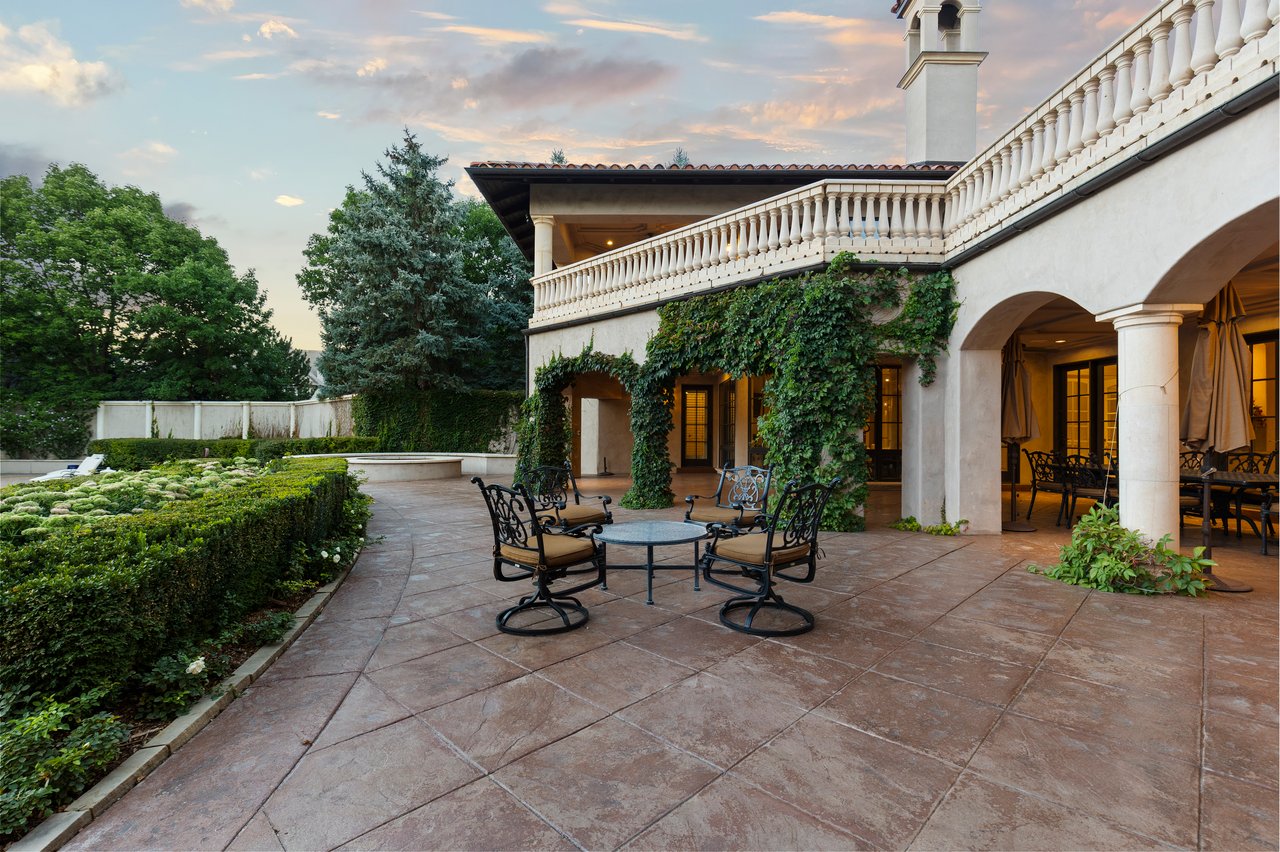 Estate courtyard patio with wrought-iron seating, manicured gardens, and ivy-covered walls.